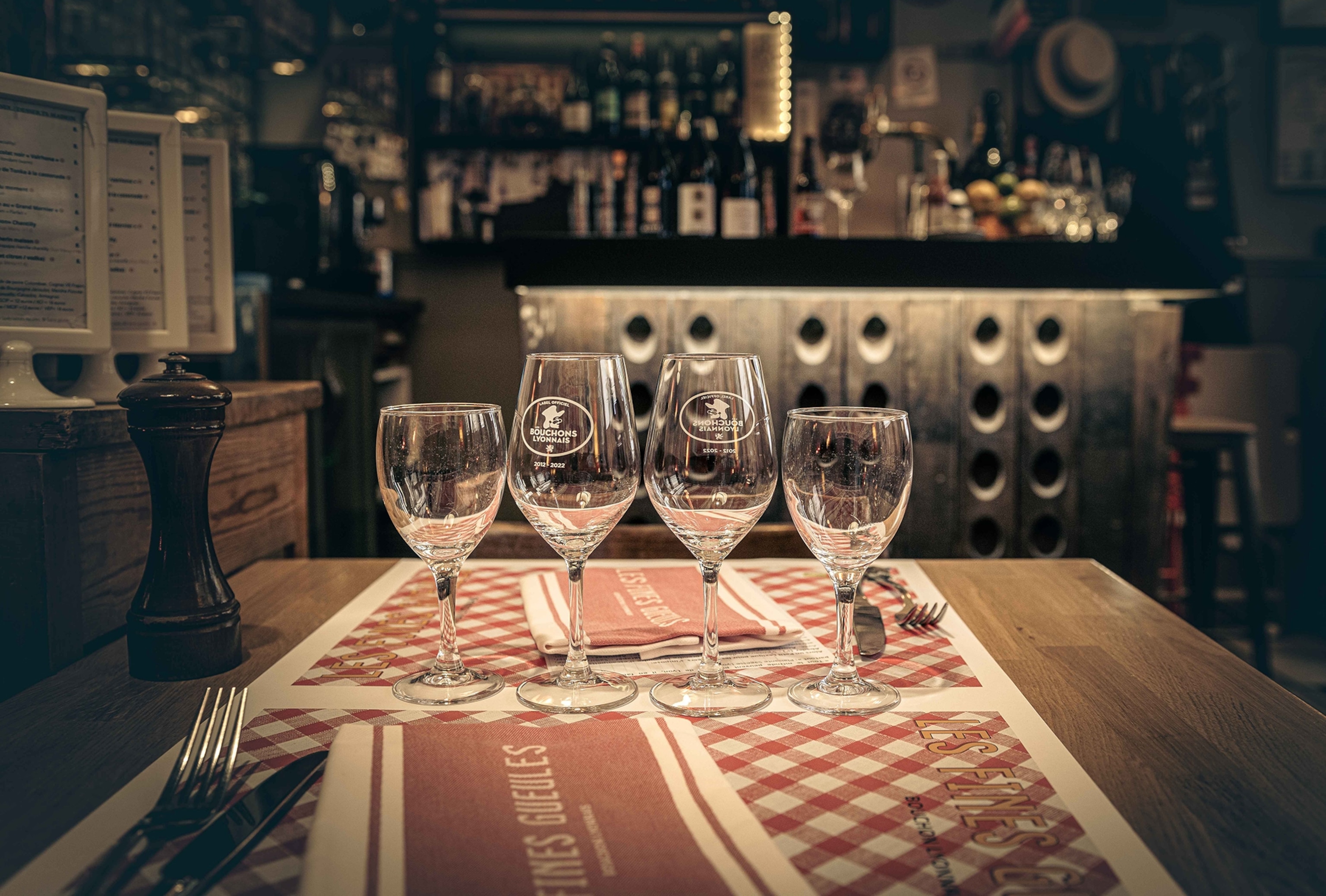 A wide table shot with four wine glasses lined up in the foreground and a warm, dark cavern-like restaurant in the background.