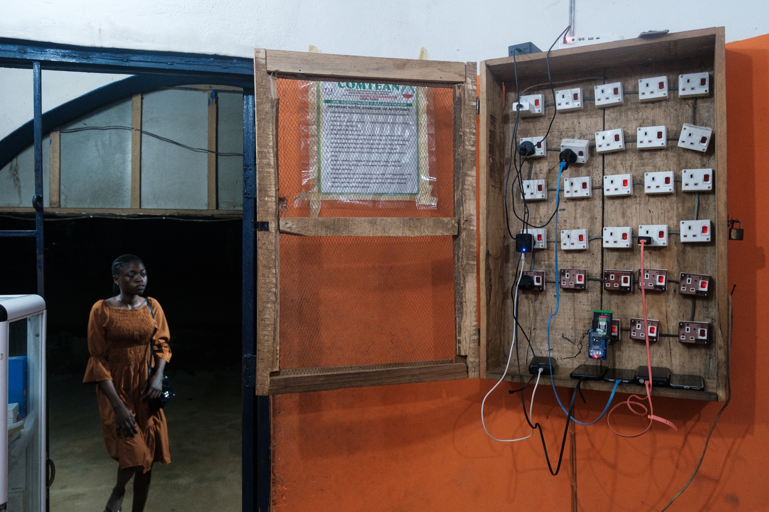 A woman stands in the doorway of room that features a cabinet of charging outlets.