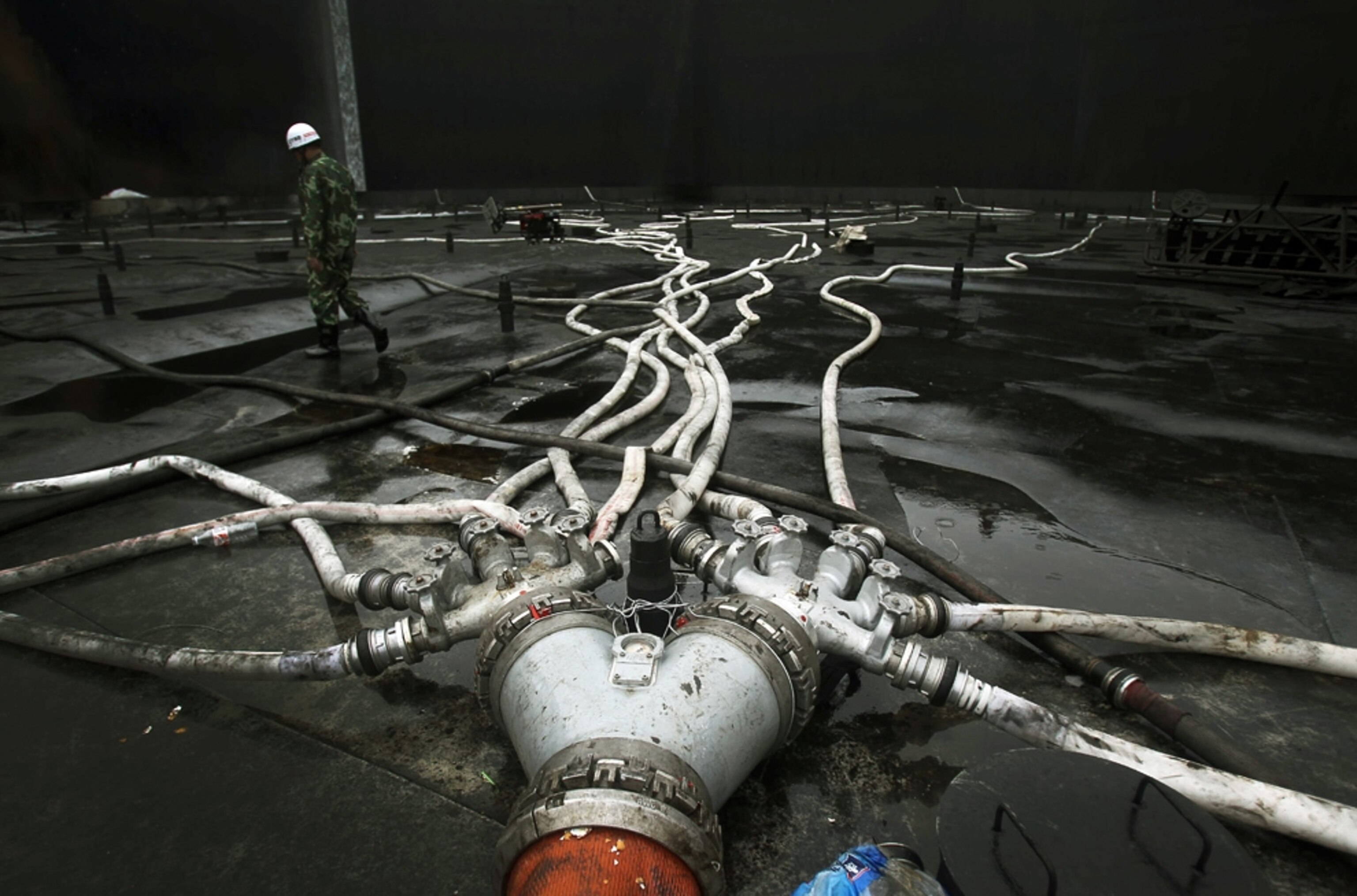 a firefighter stepping over hoses after the fire from the explosion that had spawned the China oil spill in Dalian was extinguished.