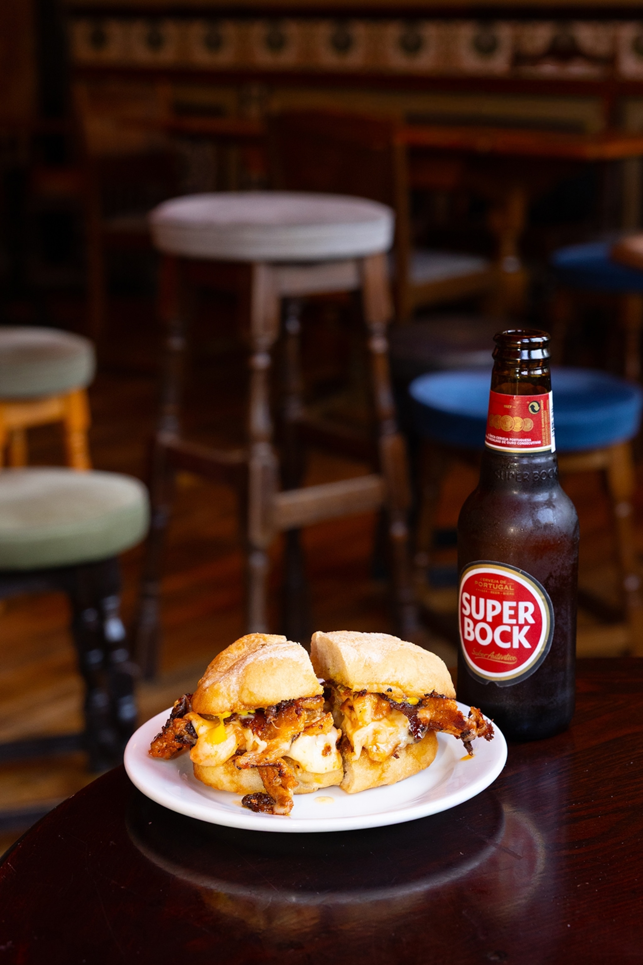 A sandwich with pork and cheese on a pub table with a beer bottle on the side.