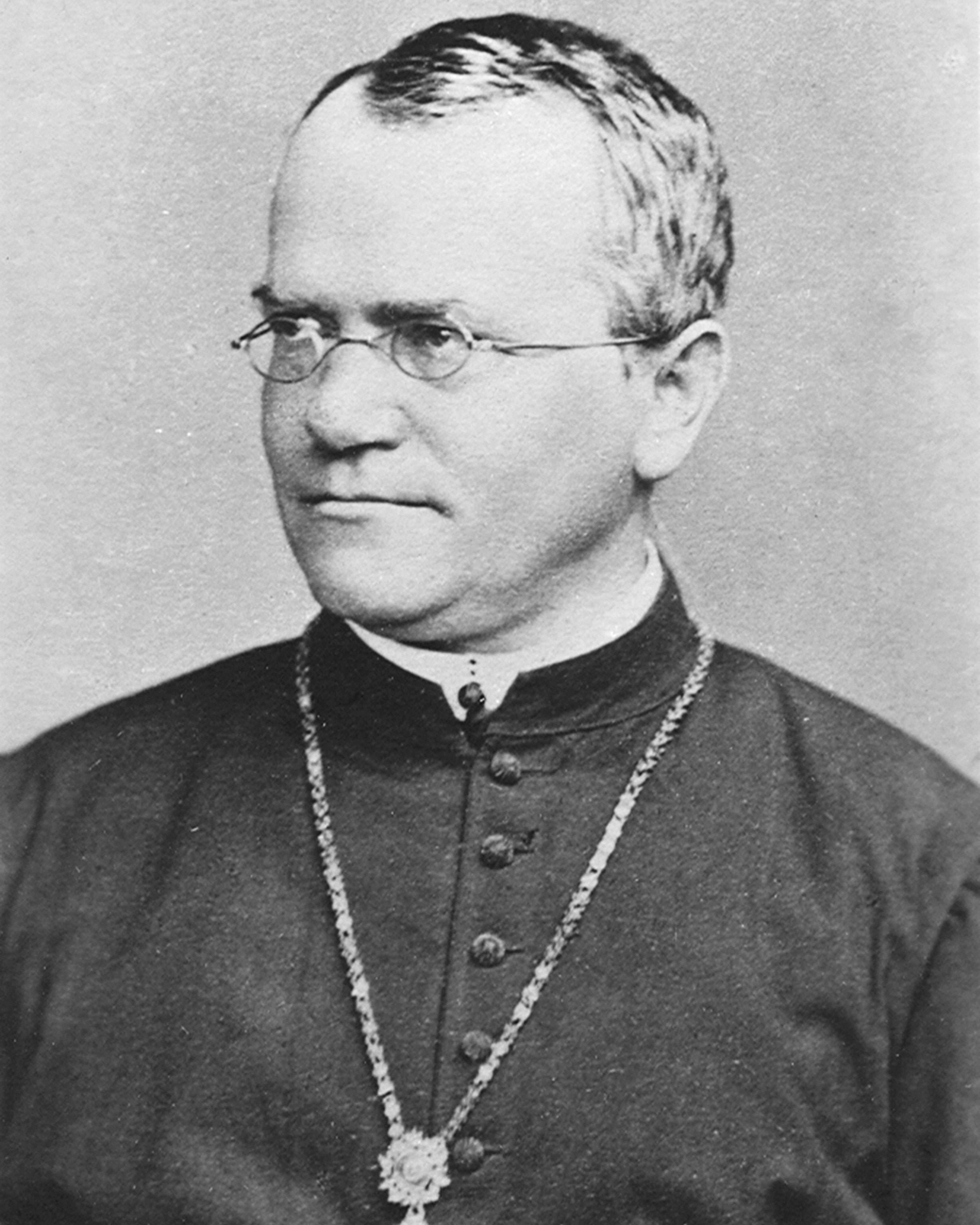 Black and white portrait of a man with glasses, wearing a dark clerical robe with buttons and a large cross necklace.
