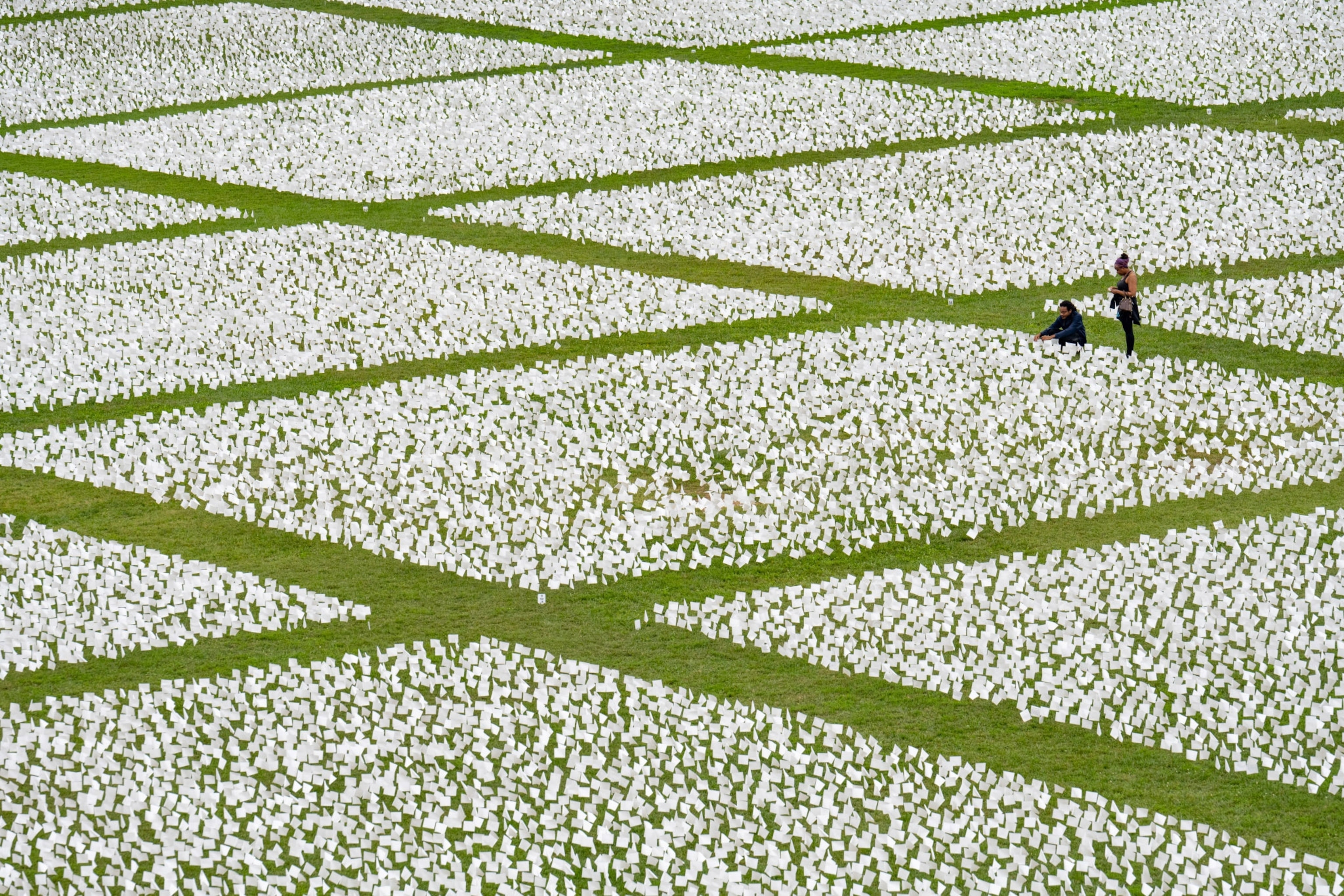 people walking near the Covid-19 memorial in Washington D.C. surrounded by white flags on the green lawn.