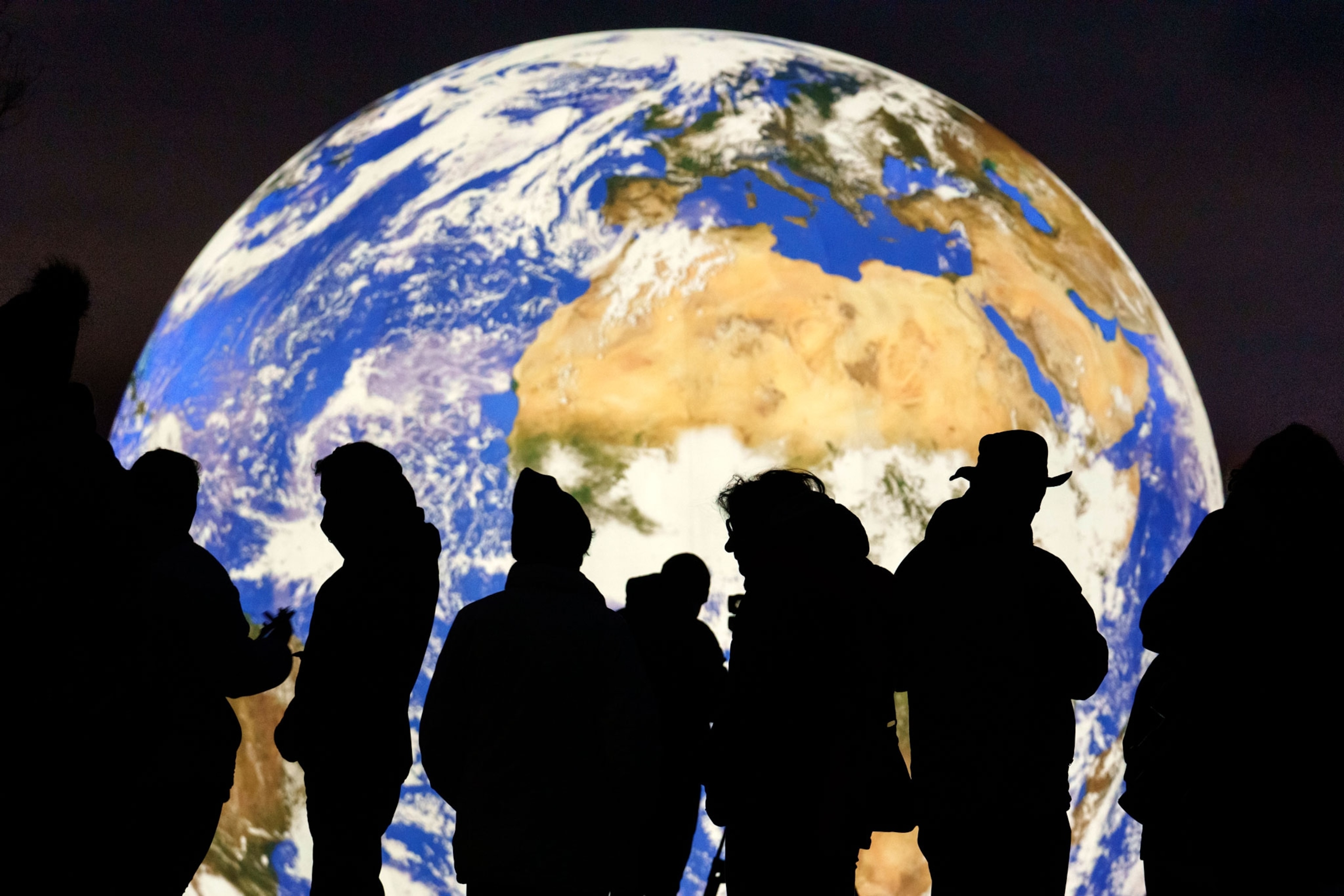 the silhouette of people can be seen as a giant glowing earth floats on a lake