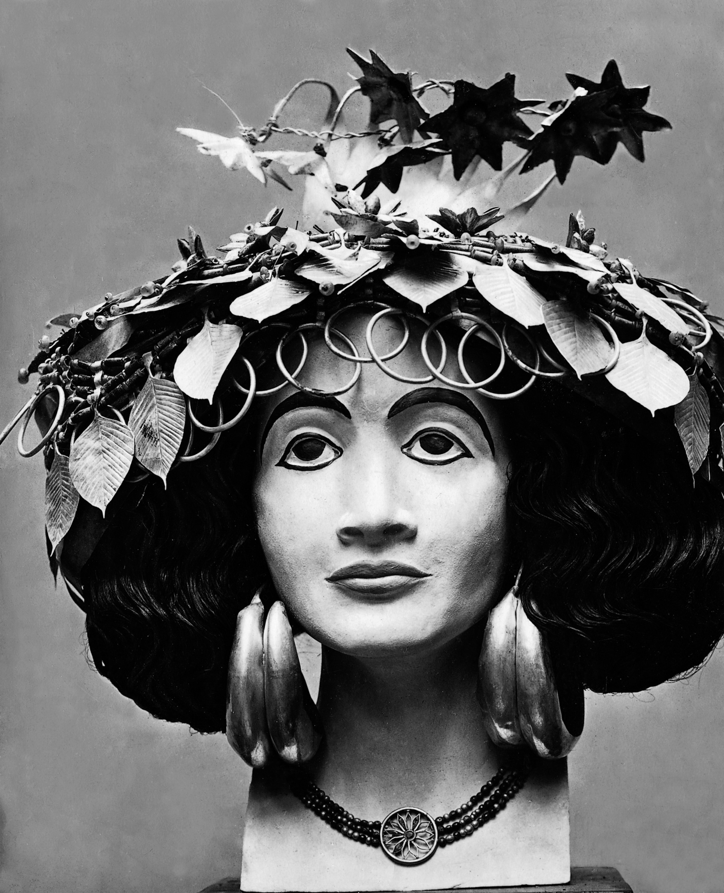 Black and white photo of a stylized bust with an elaborate headdress of leaves and loops.