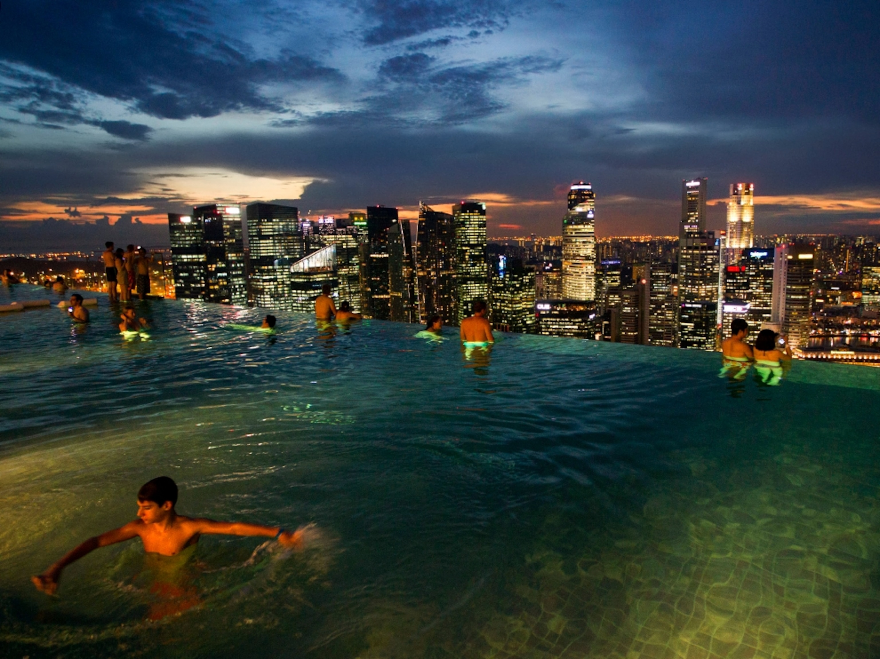 people swimming on a rooftop pool at night in Singapore