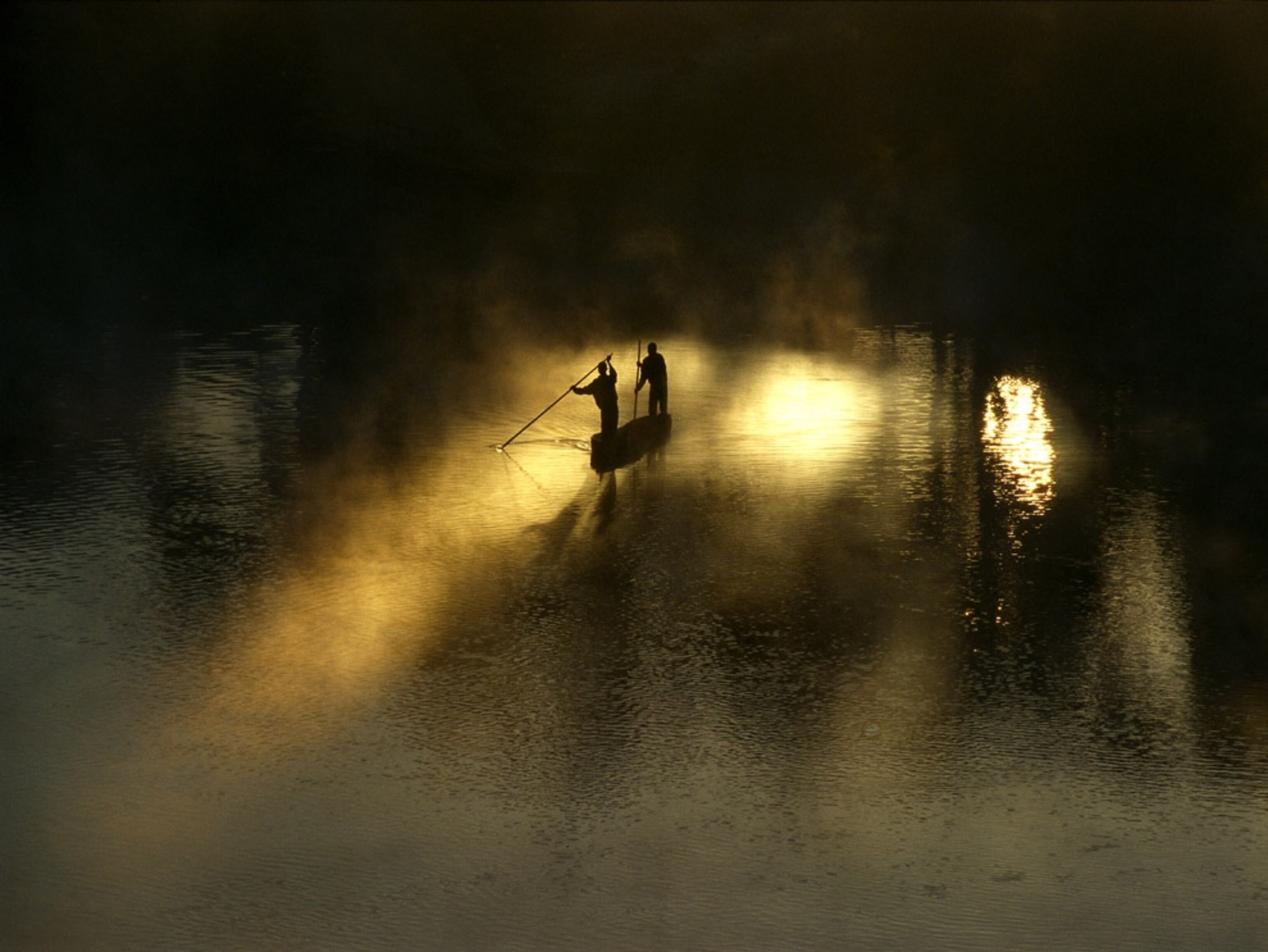 Men paddle in a dugout canoe at dawn on the Zambezi River