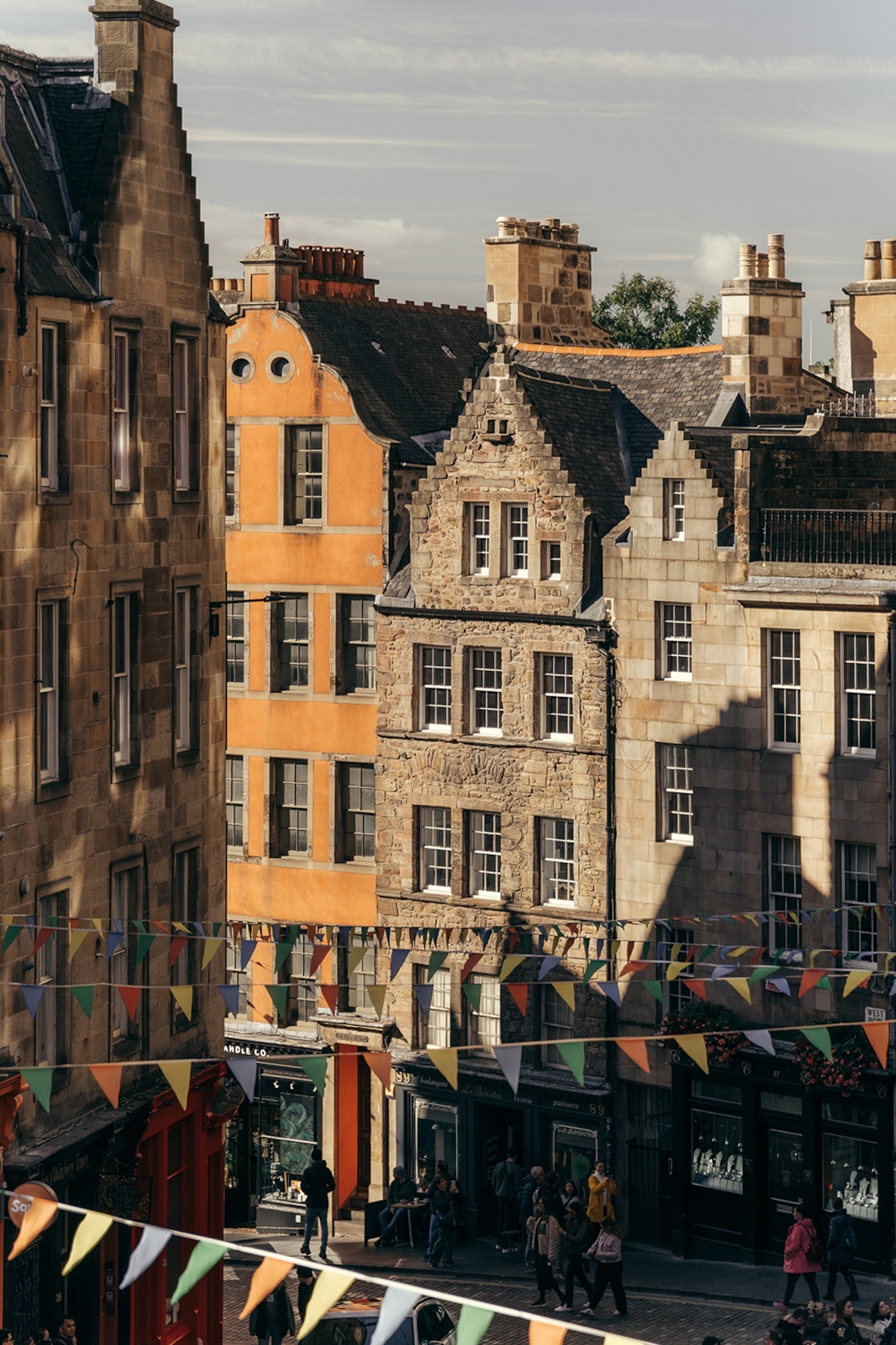 An elevated view onto a charming and narrow shopping mile in a traditional stone-housed street with bunting hung across.