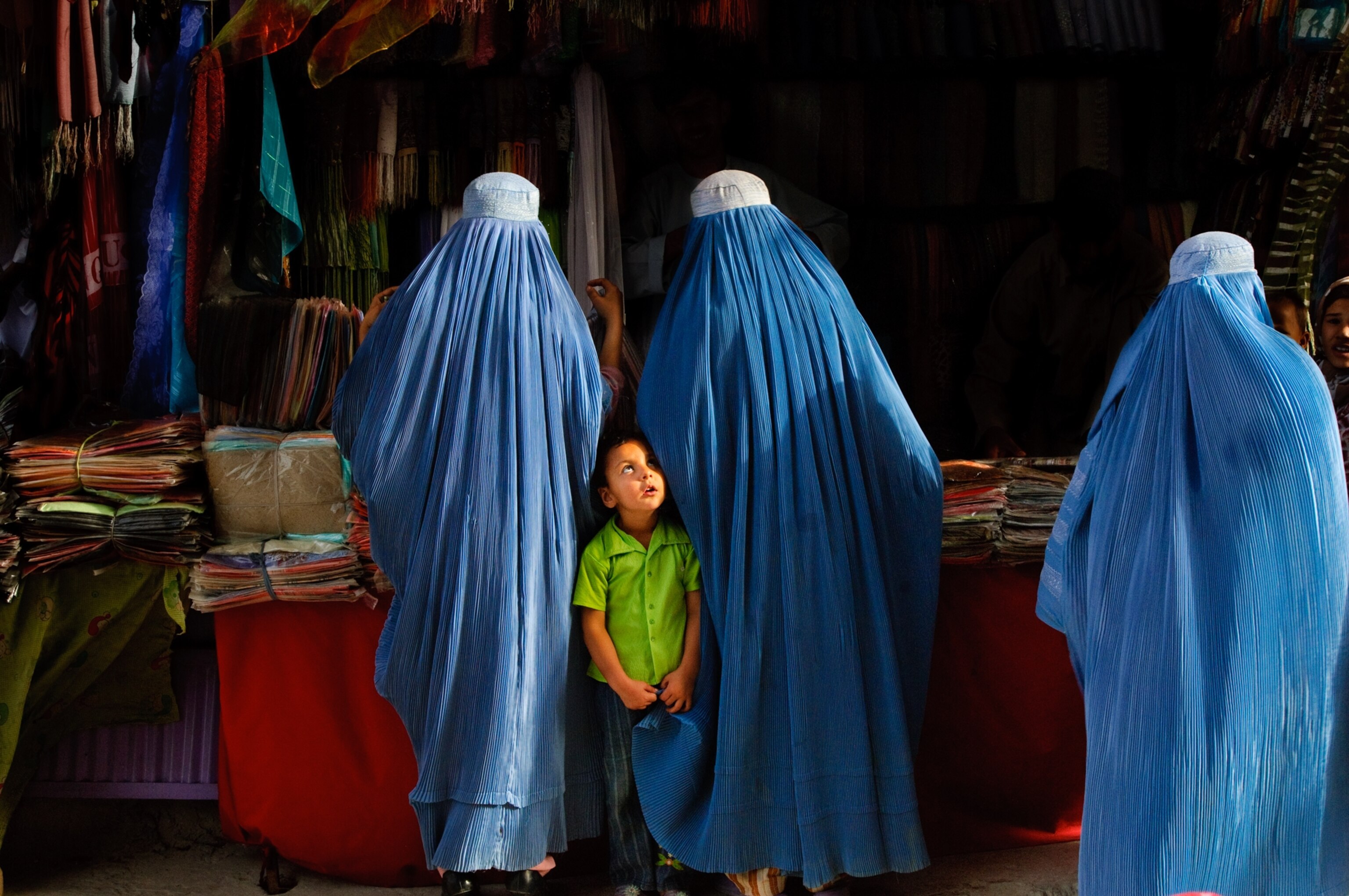 a girl standing between two women in a market in Afghanistan