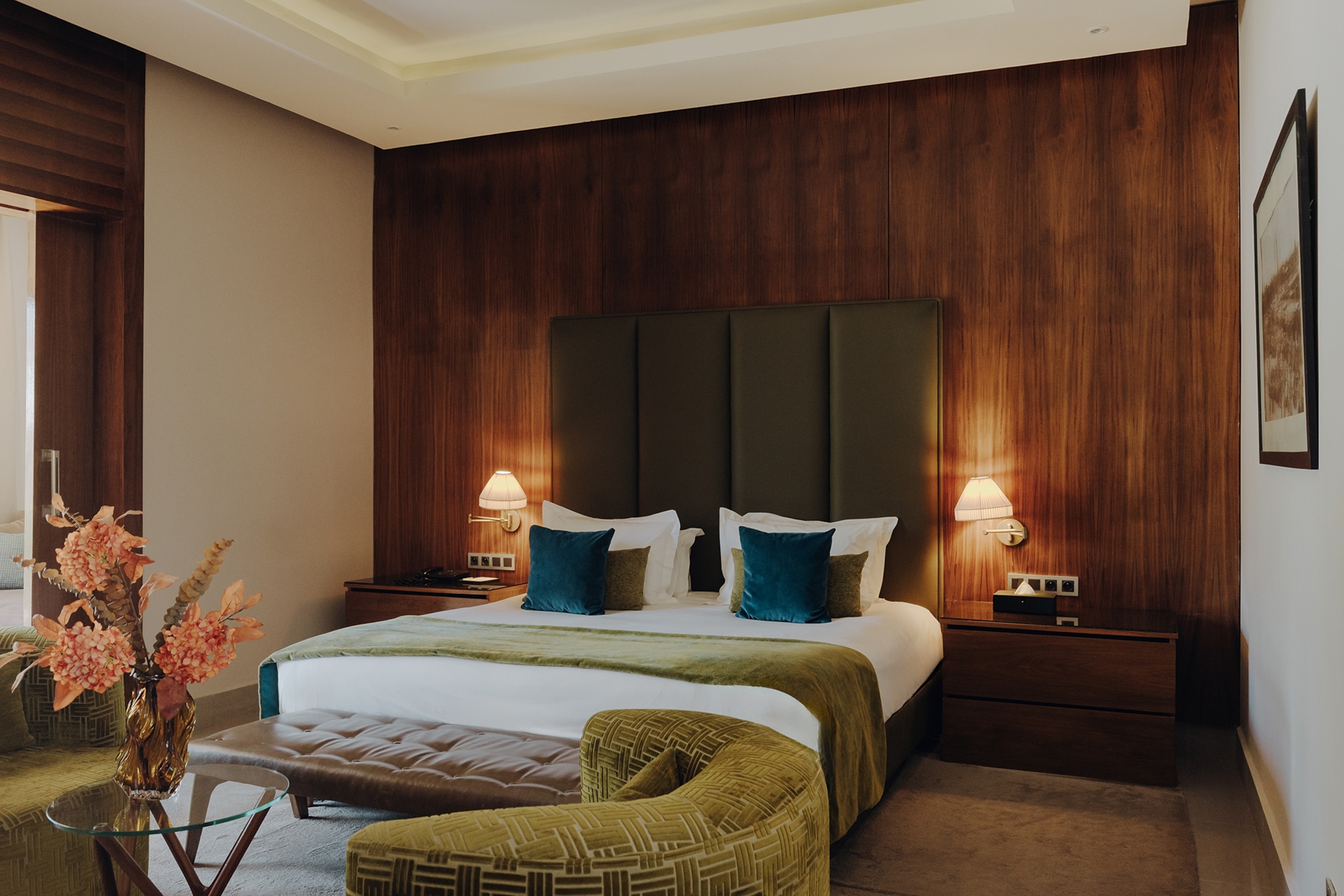 The sleek interiors of a hotel bedroom with a velvet arm chair and pillows and soft lighting.