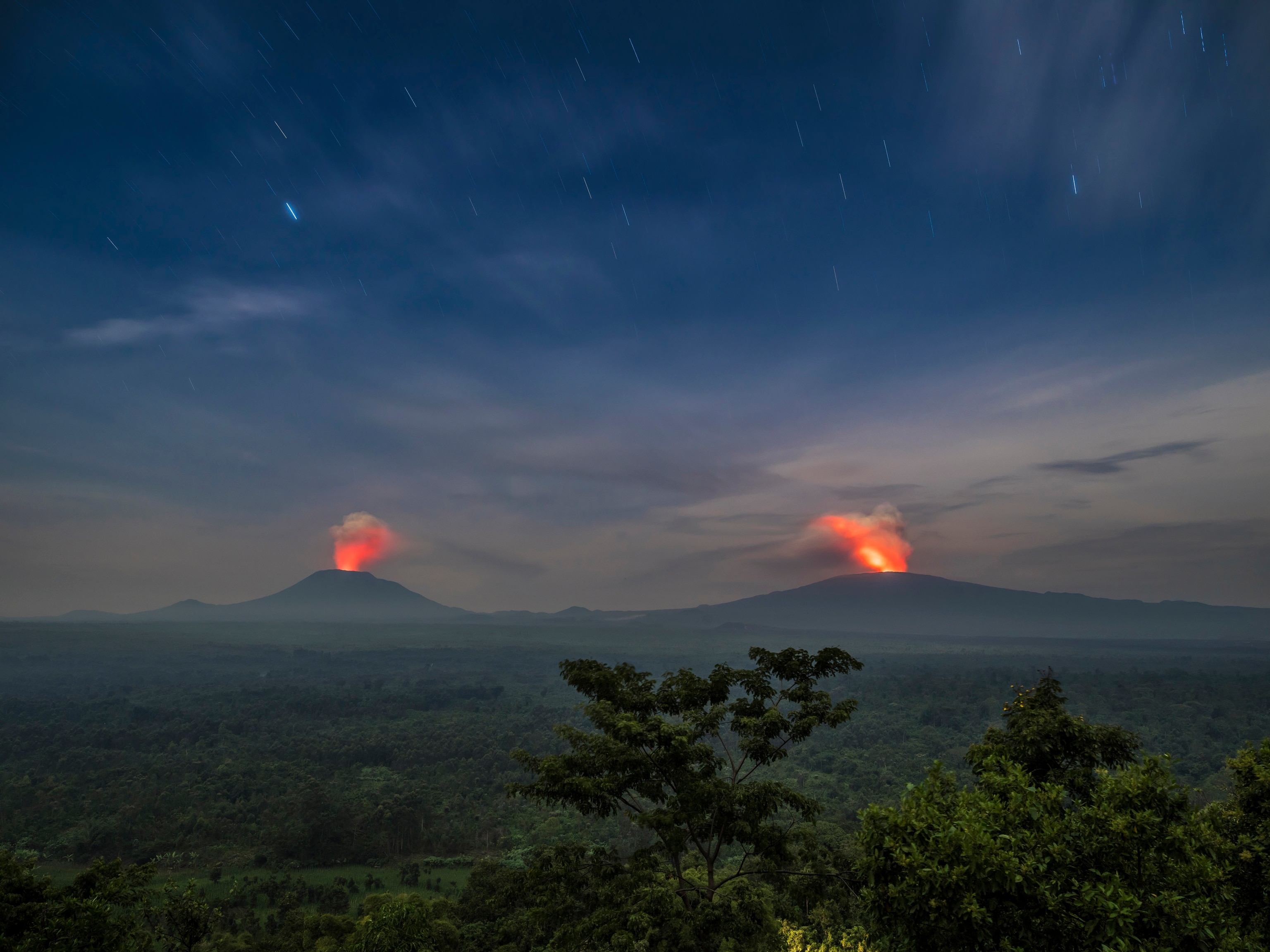 a landscape of the park at dusk with two volcanoes erupting in the background