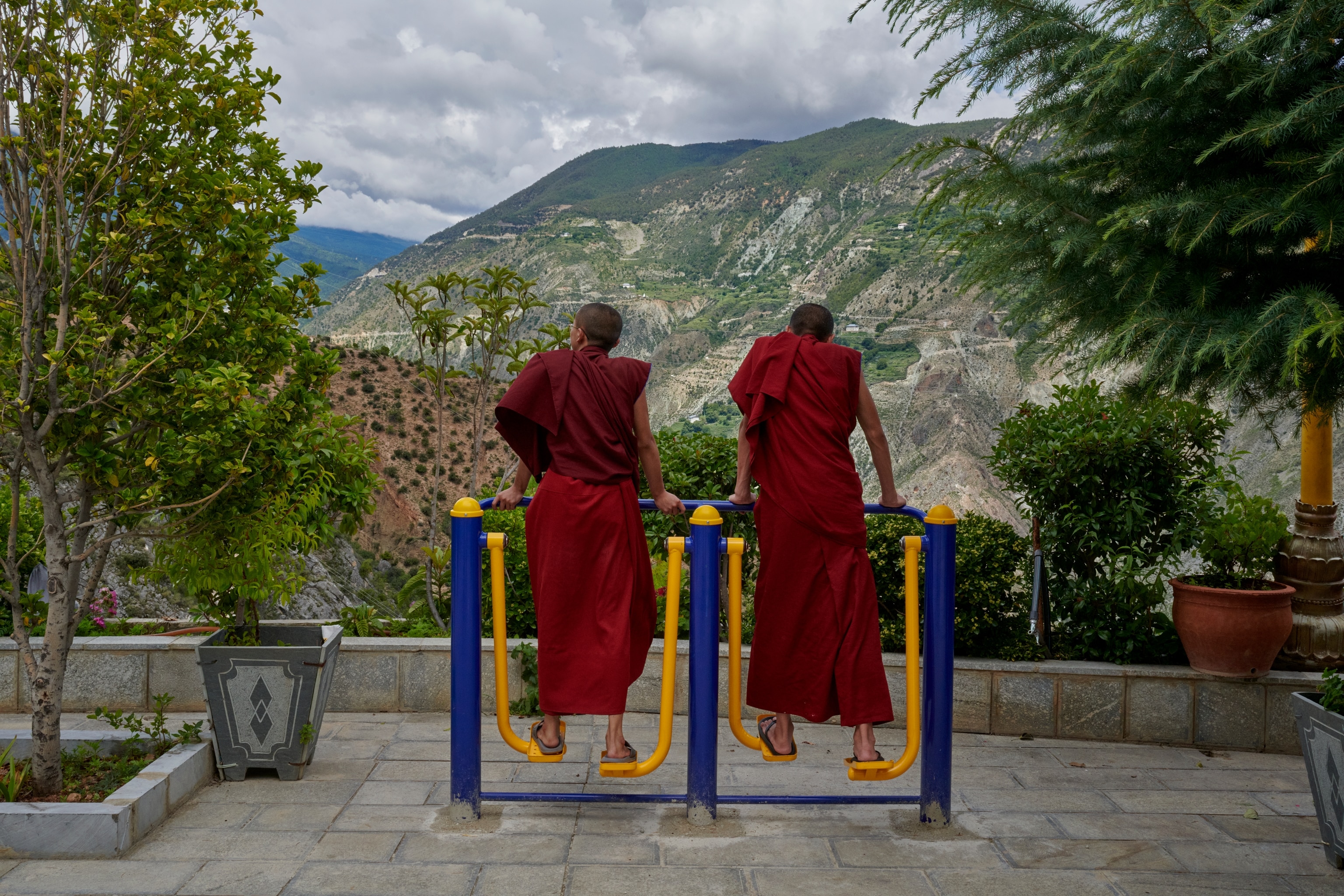 Two buddhist monks using exercise equipment with a view of mountains in front of them.