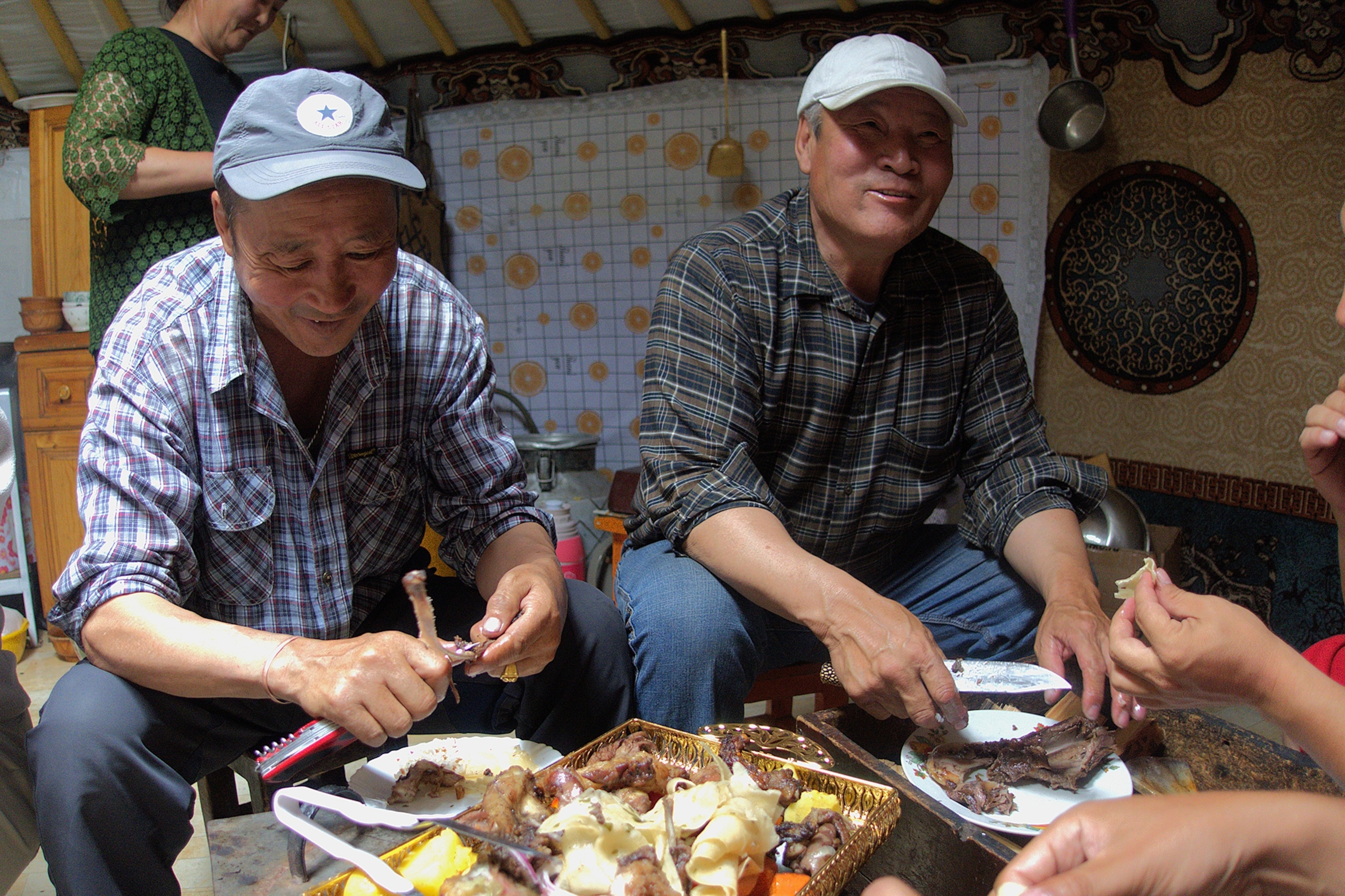 Two men tearing at a plate of mutton on the interior of a traditional nomadic tent.