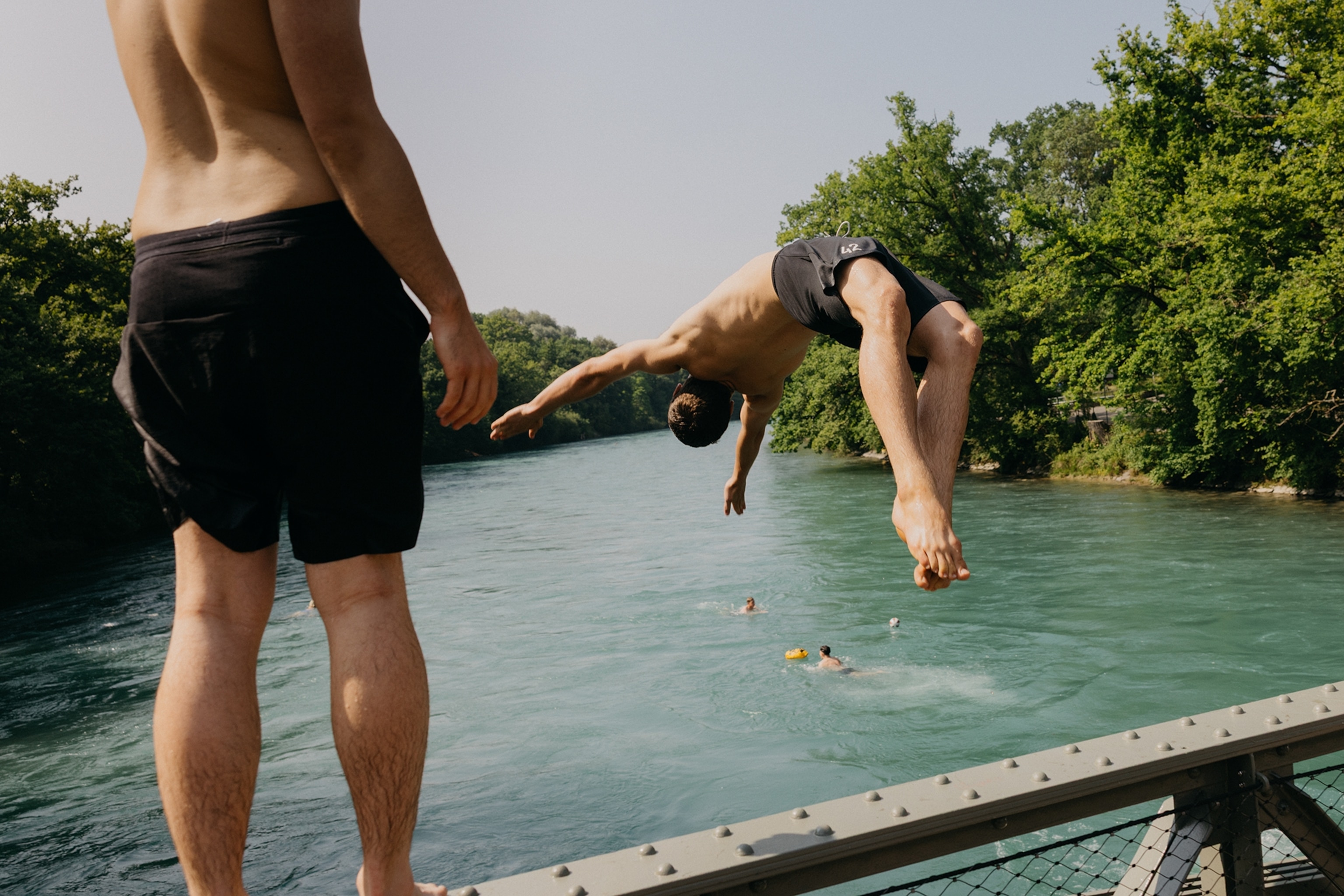 A couple of young people performing a backflip jump into a river.