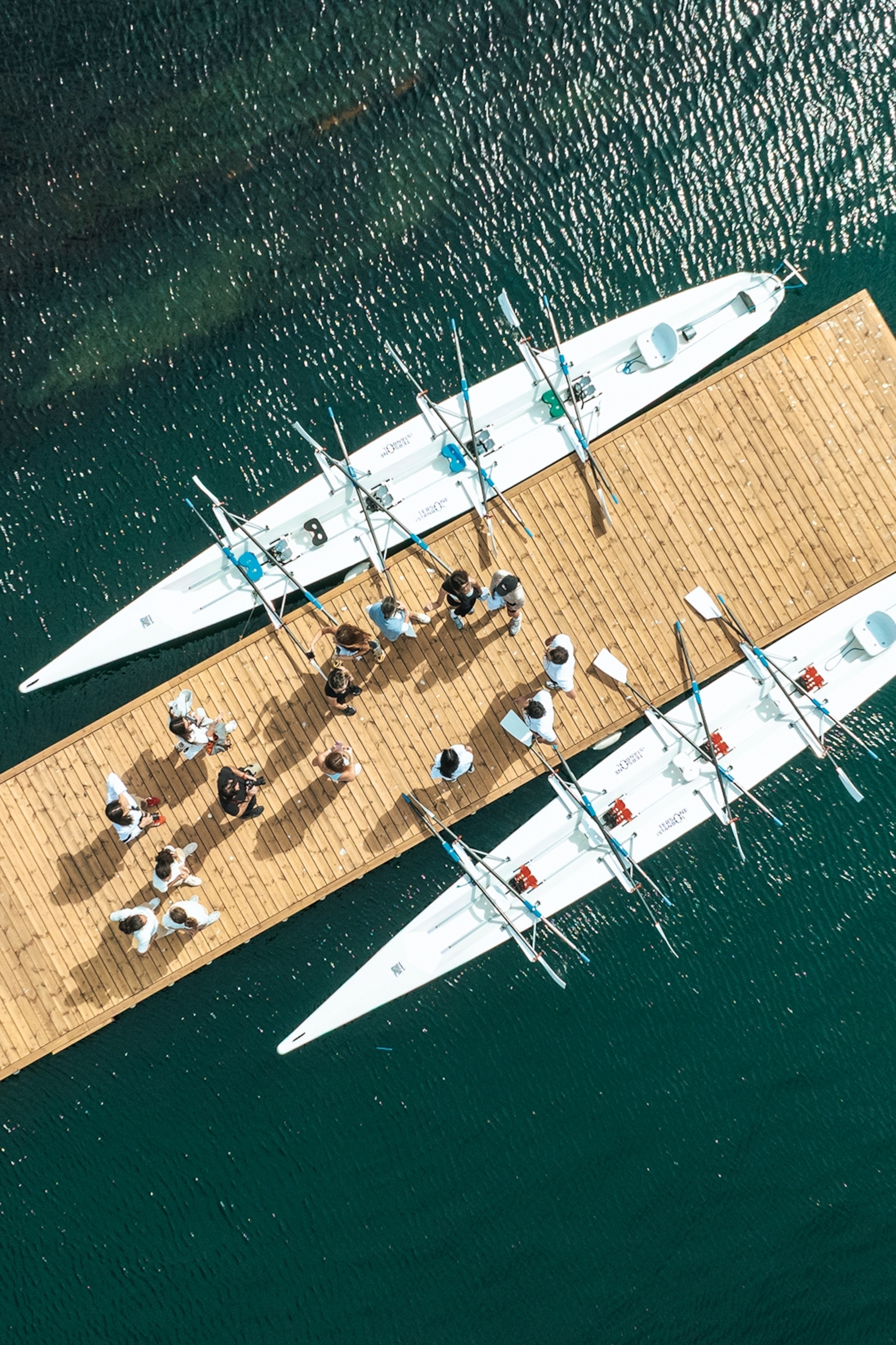 A birds-eye view onto a busy pier with two rowing boats lined up on either side of the wooden pier.