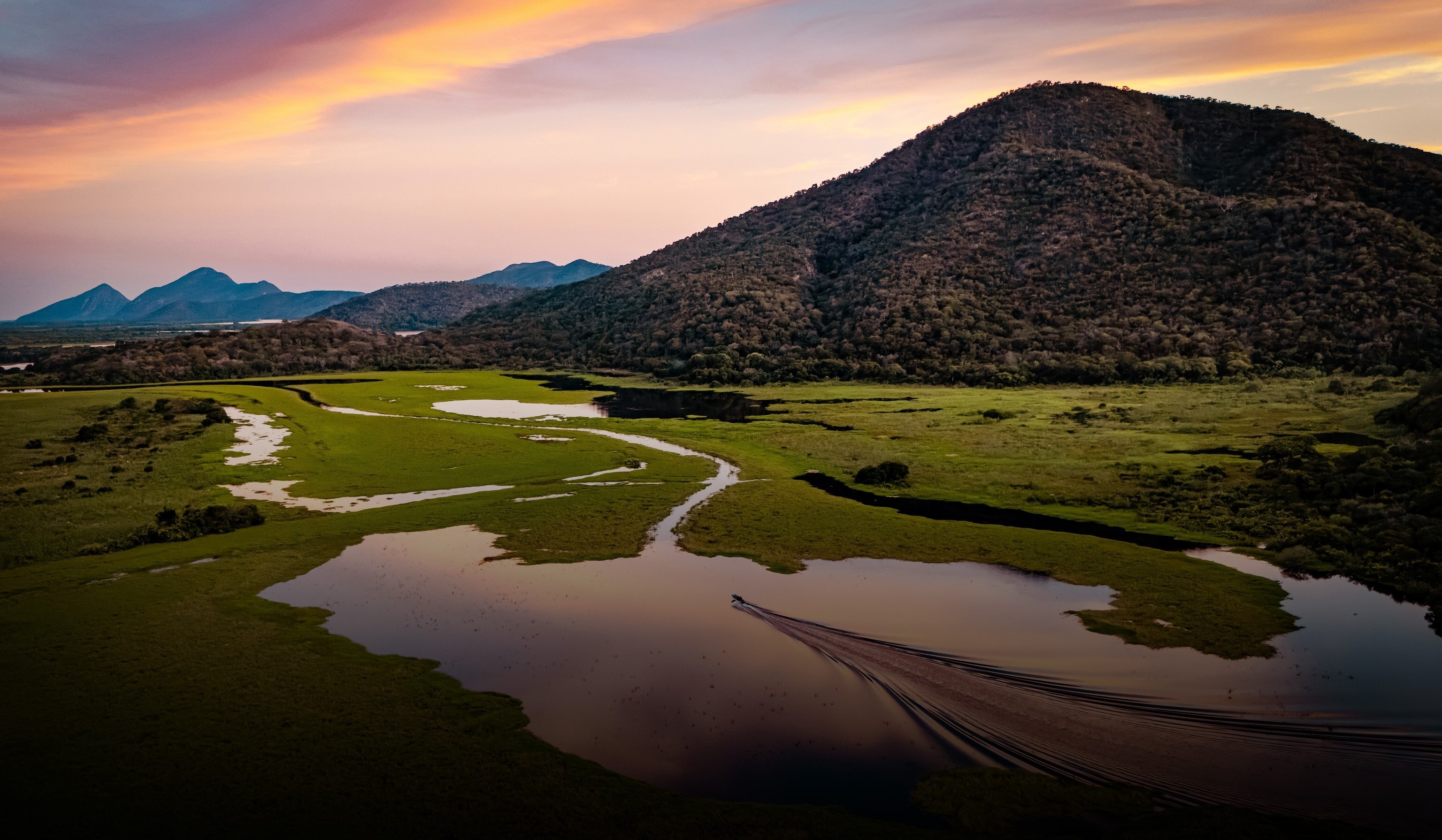 In the soft light of sunset, a boat carving path through the winding river.