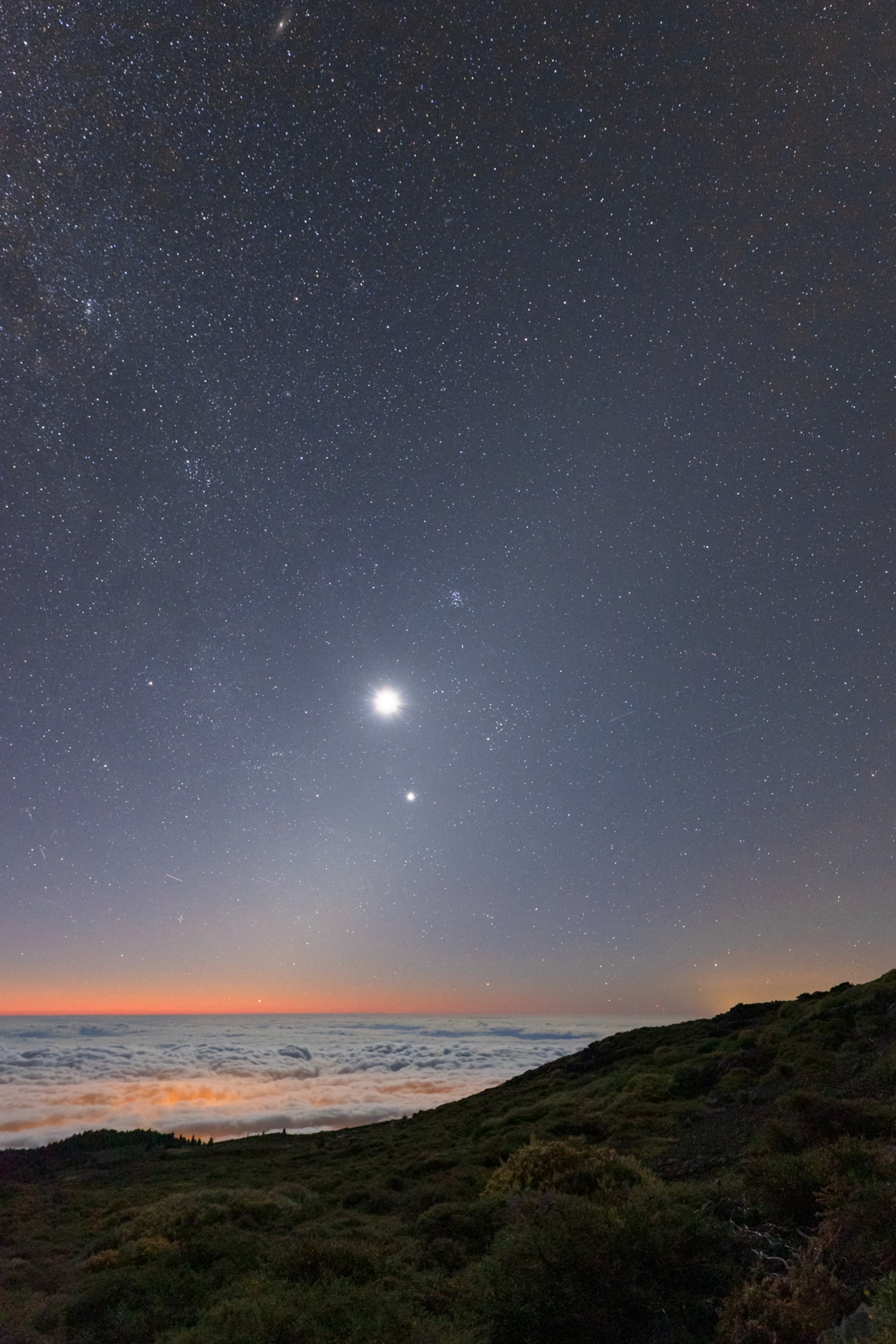 Night sky over a coastal landscape with a starry sky, two bright celestial objects aligned vertically