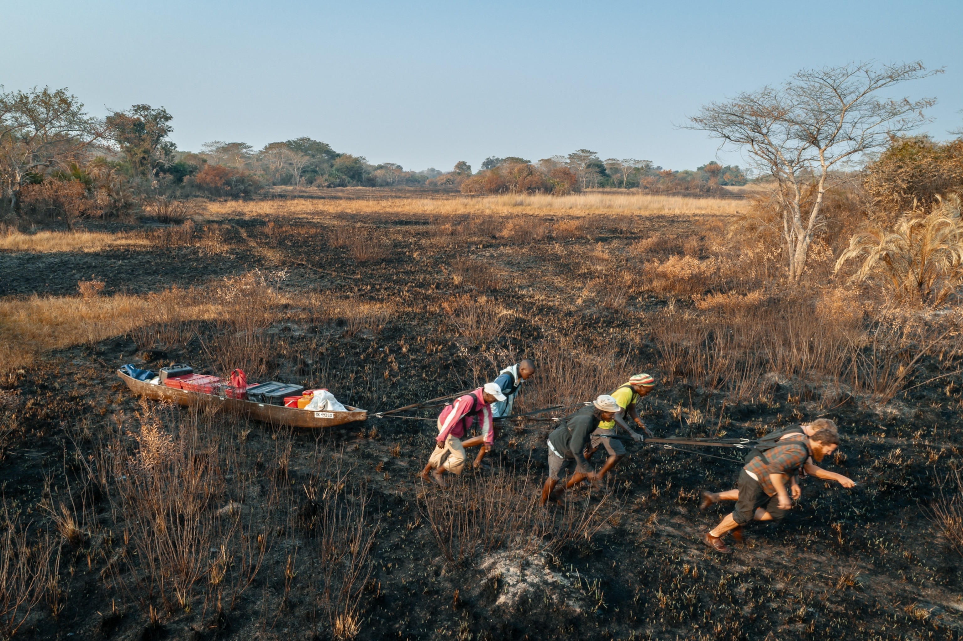 Six-person team using harnesses to pull the boat over burned floodplains during the dry winter months.