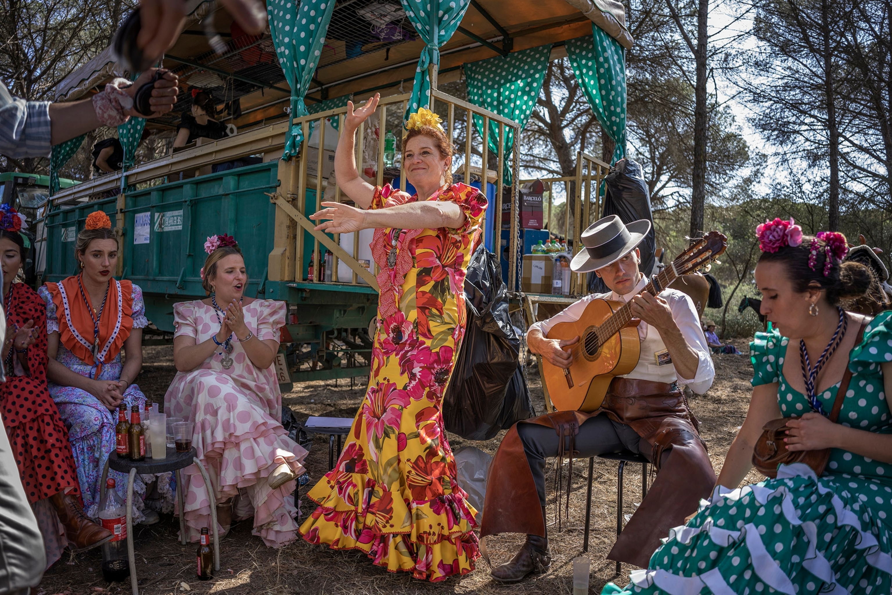 A woman in a colorful floral dress dances surrounded by a man playing guitar and other onlookers.