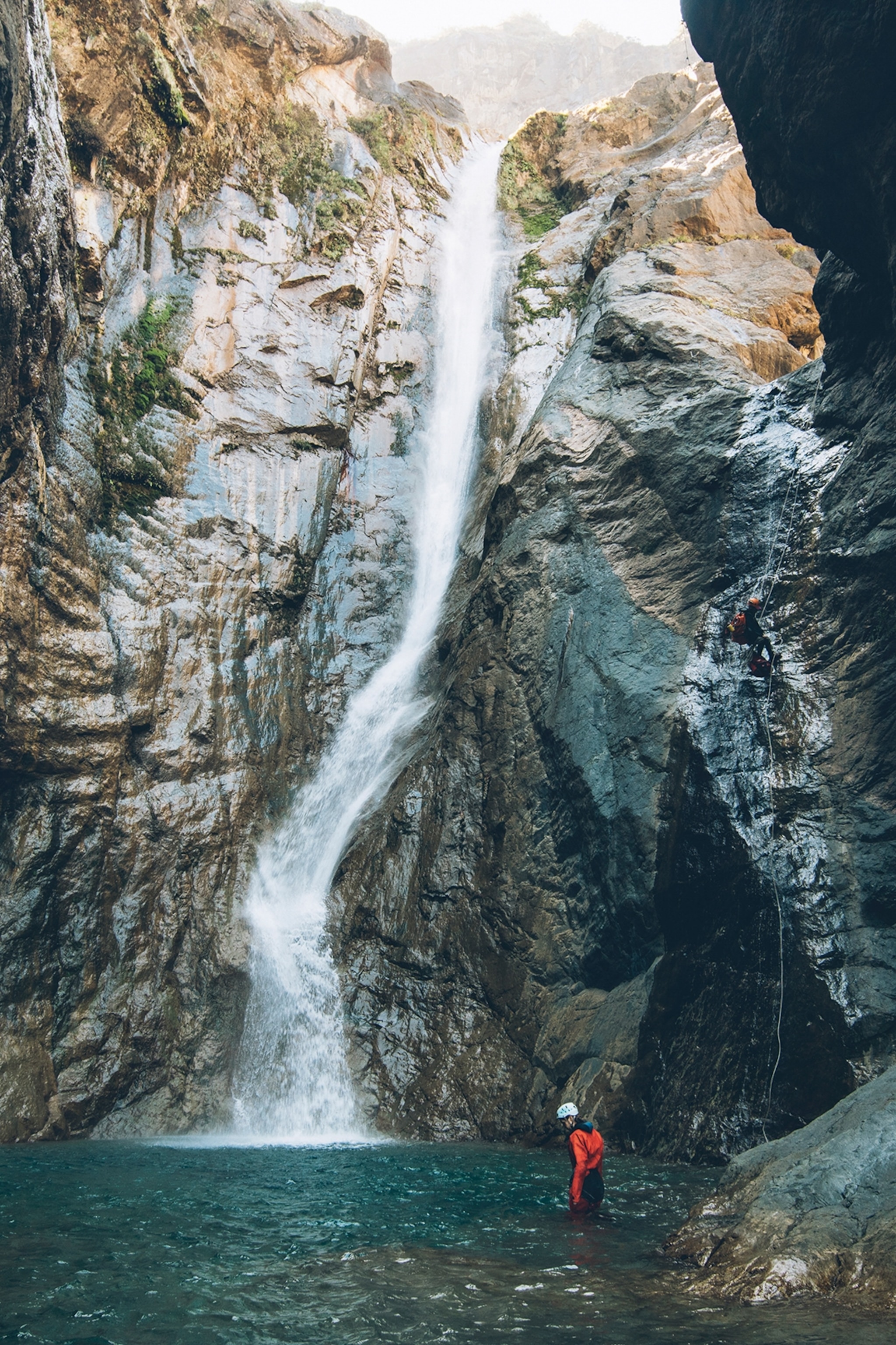 A dramatic open cave with a waterfall plummeting into a natural pool below.