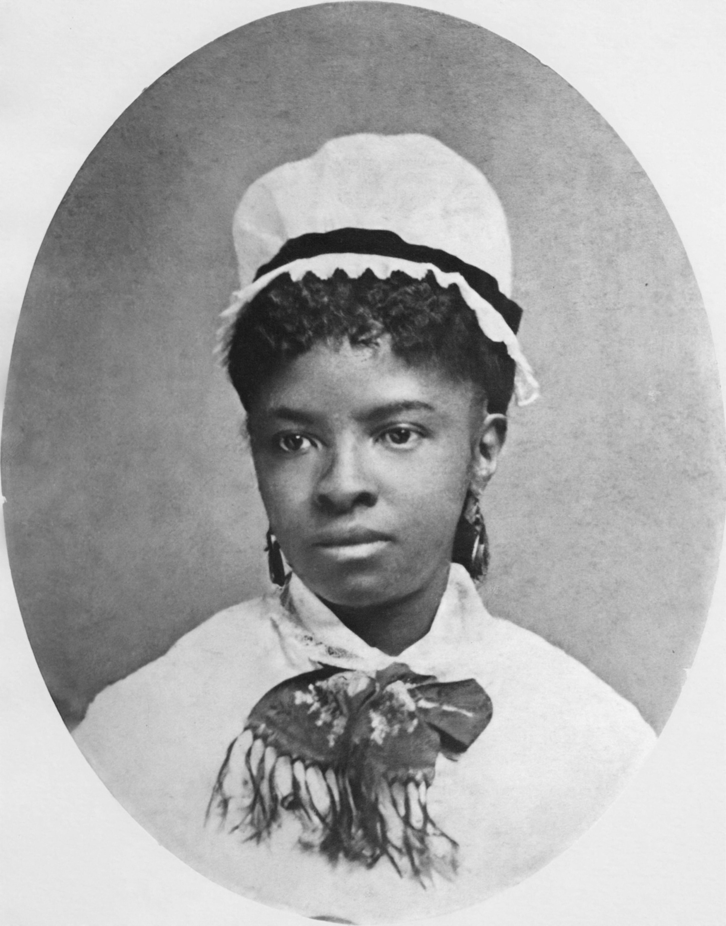 A black-and-white photos of a young woman wearing a white cap and a floral scarf