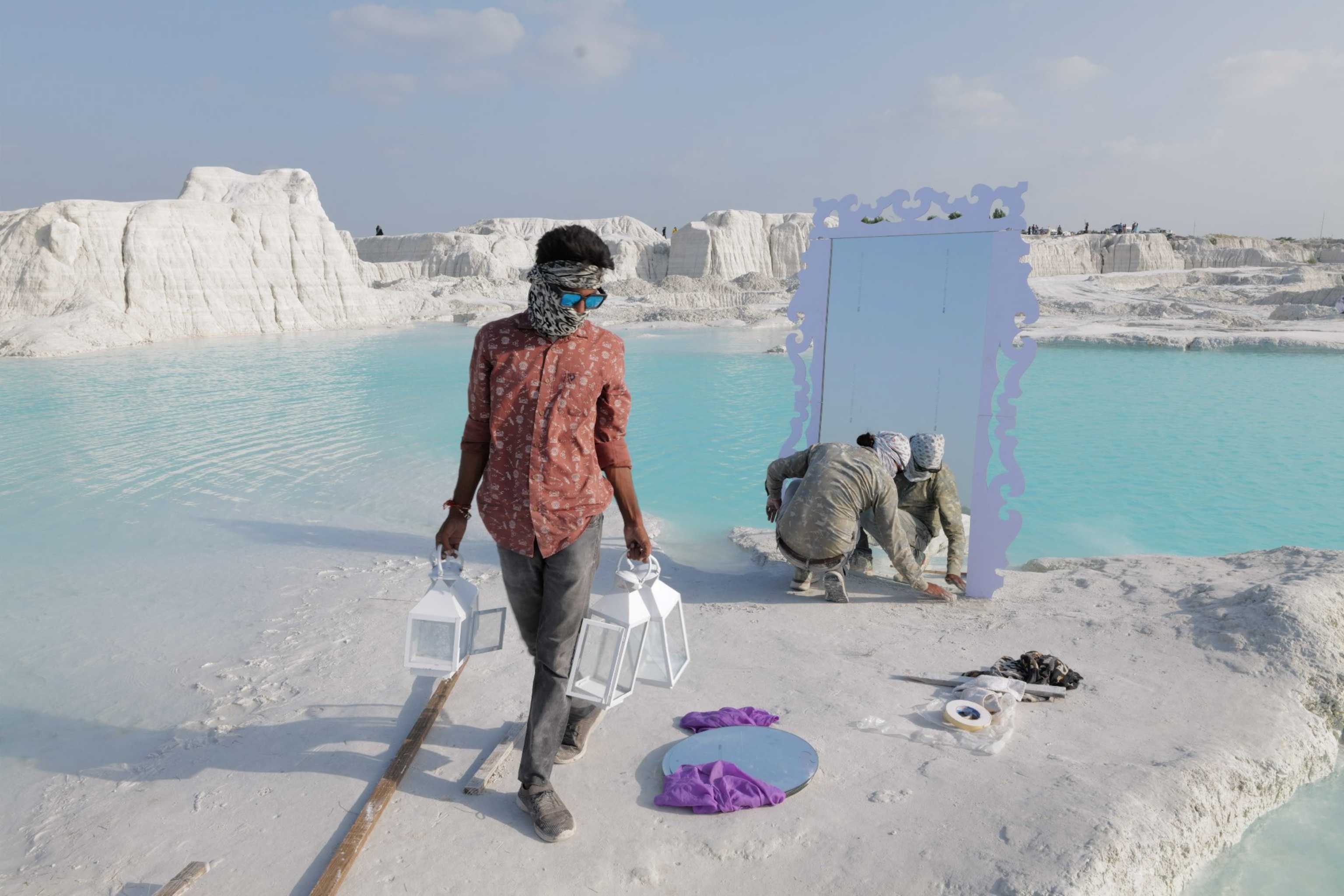 A man carries two objects in his hands while another sets a mirror up.