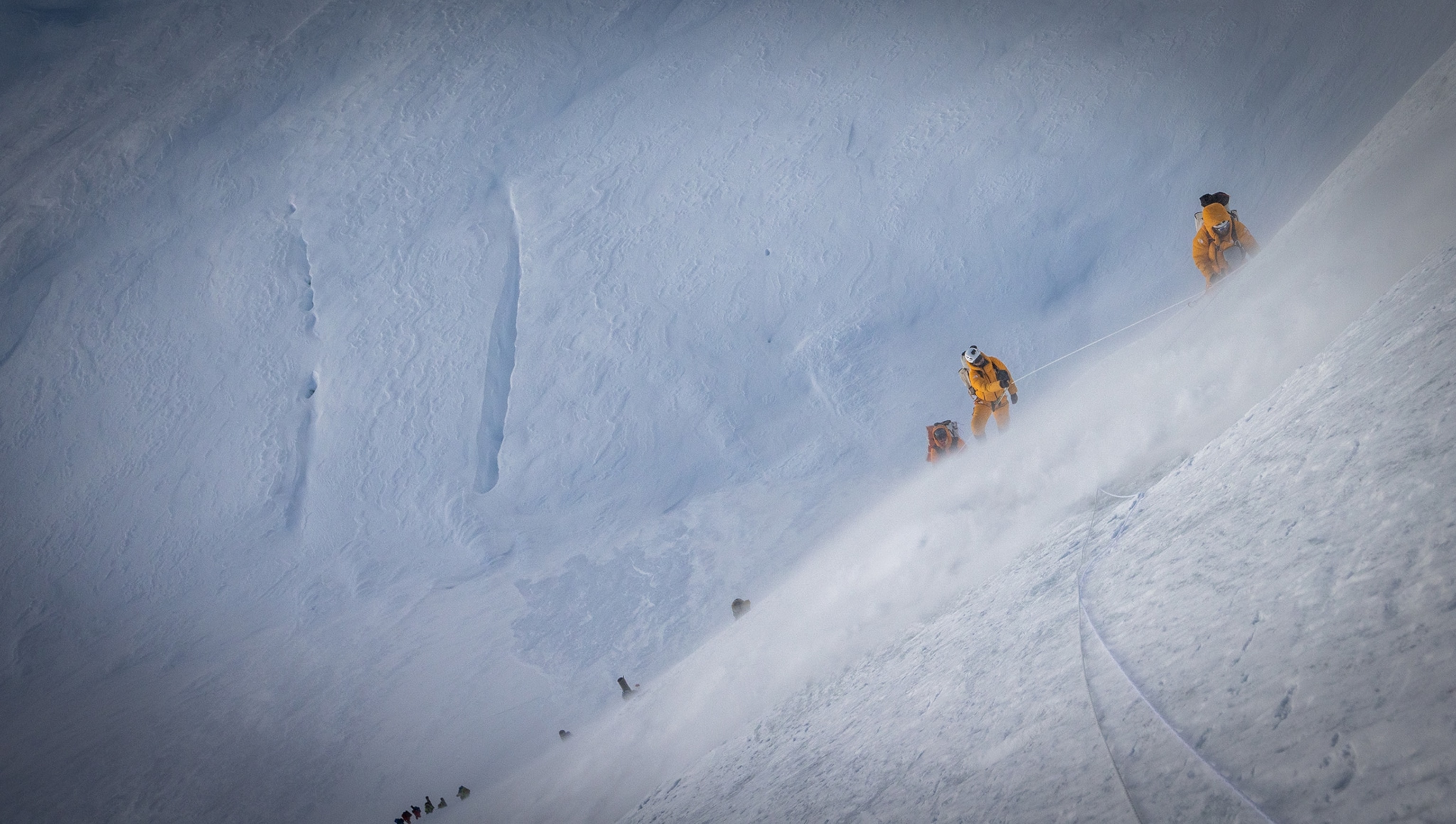 Three skiers climb the side of a snowy mountain