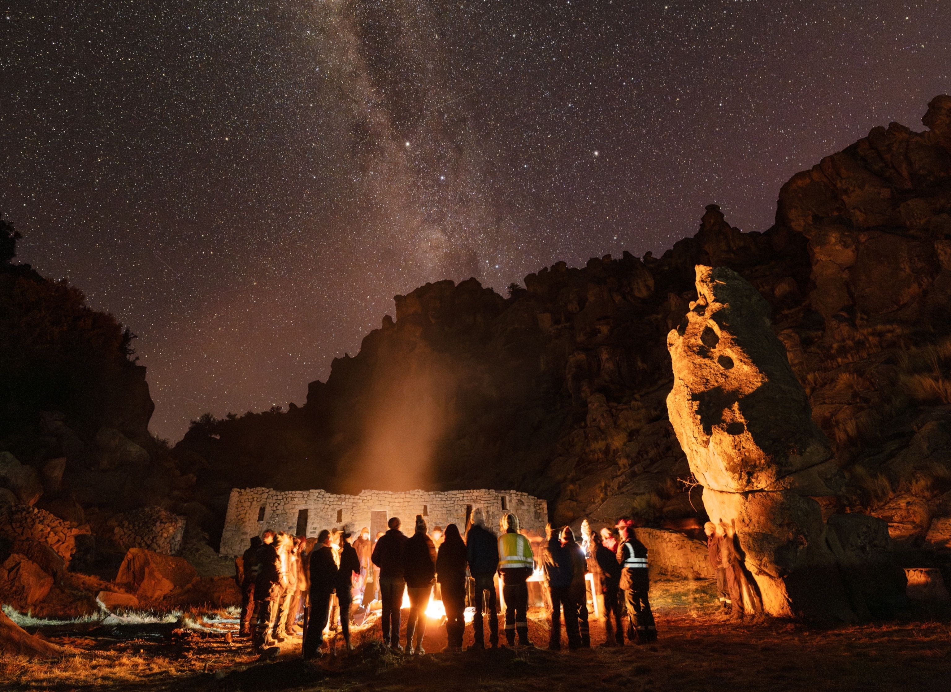 Large group of people forming a circle around fire at night.