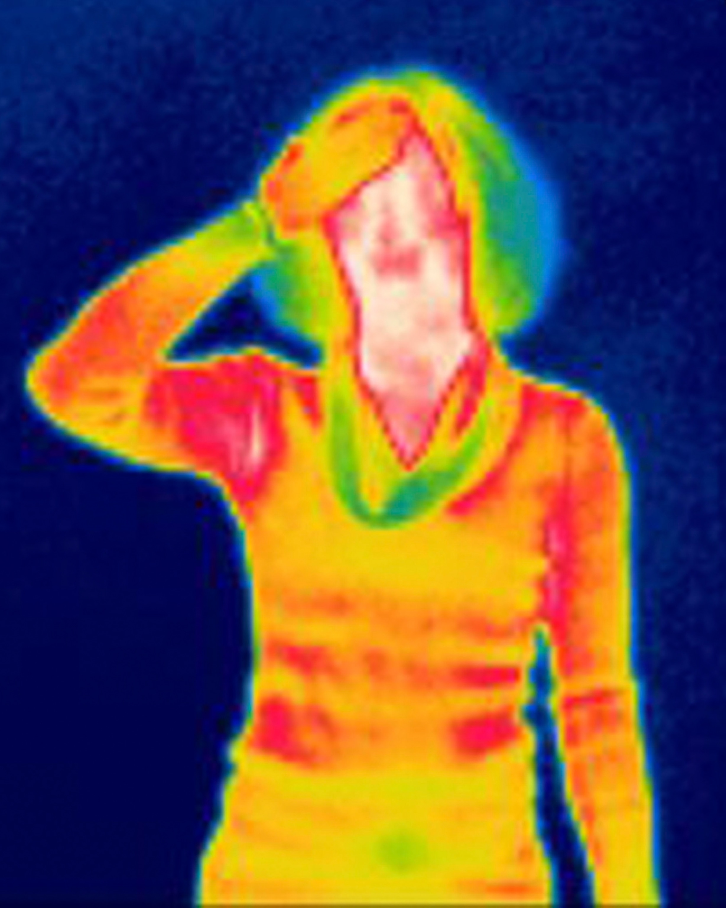 Thermal image of a person in bright colors; reds and yellows indicate heat, with a hand on their forehead