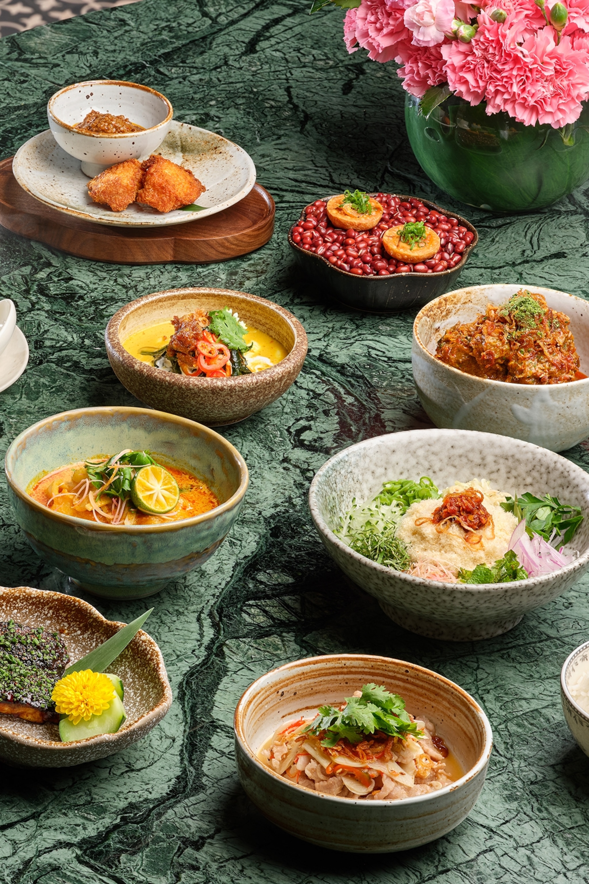 A marble table with multiple small dishes, including chicken curry and Malay satay sticks.