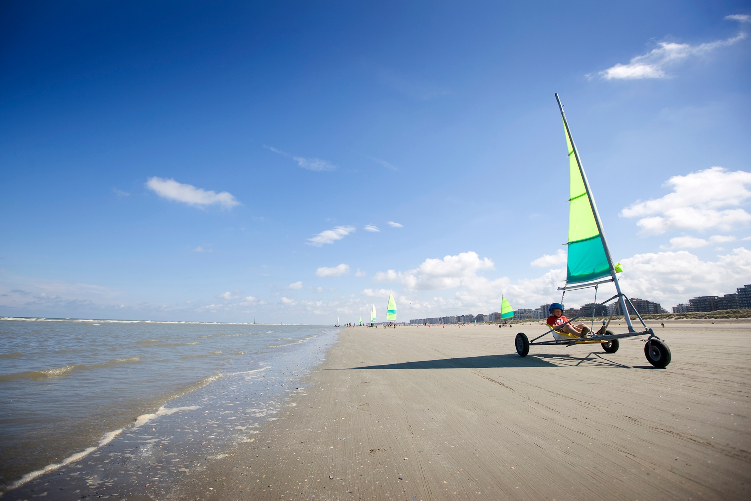 A sand sailing buggy drives by the water on the beach.