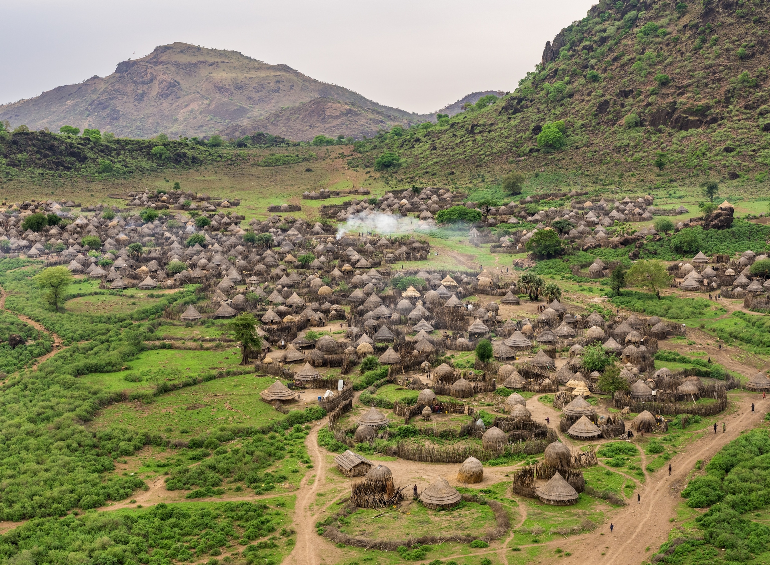 A small town sits on a green, grassy area between hills.