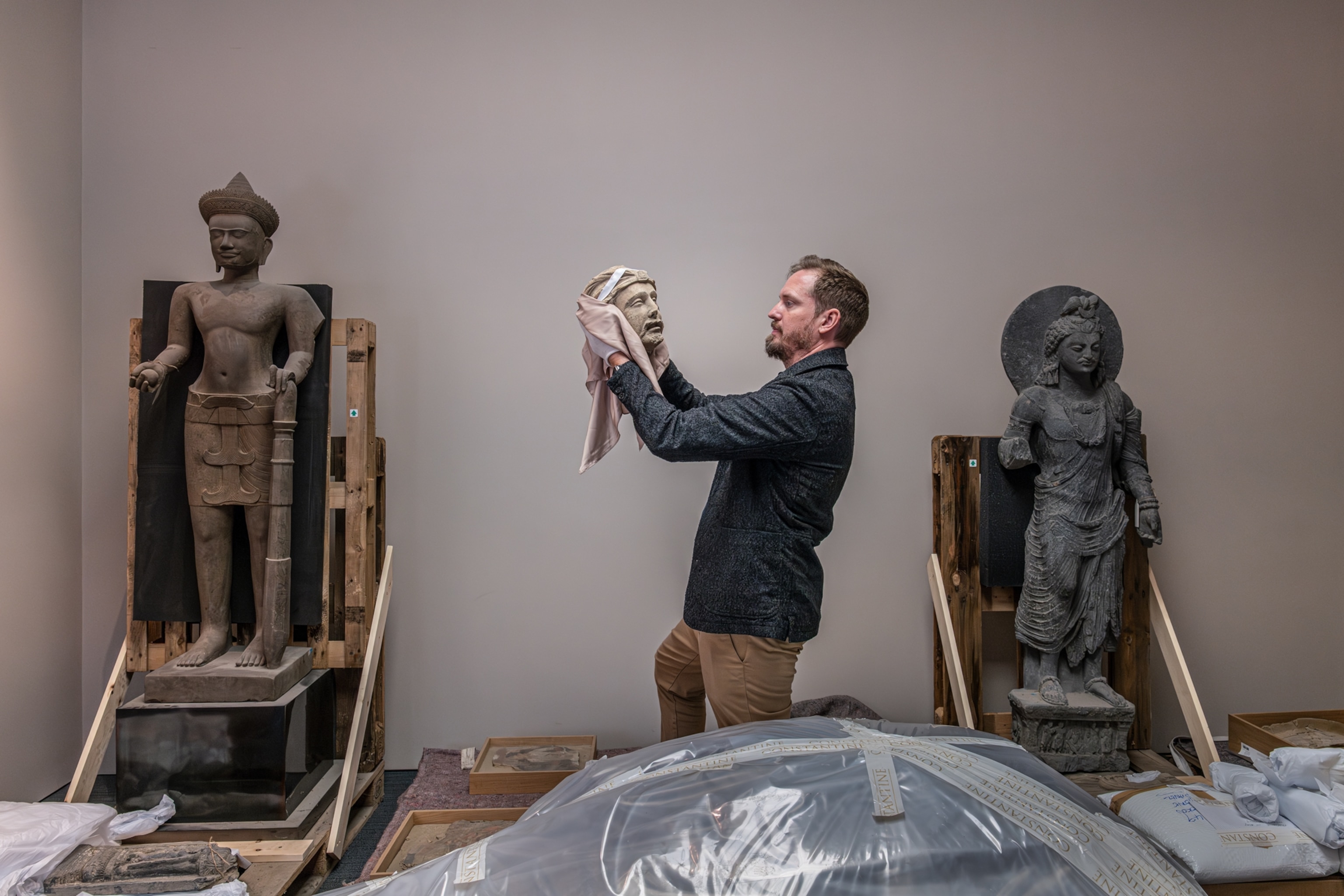 An archeologist holds up a statue head in a room surrounded by other artifacts.