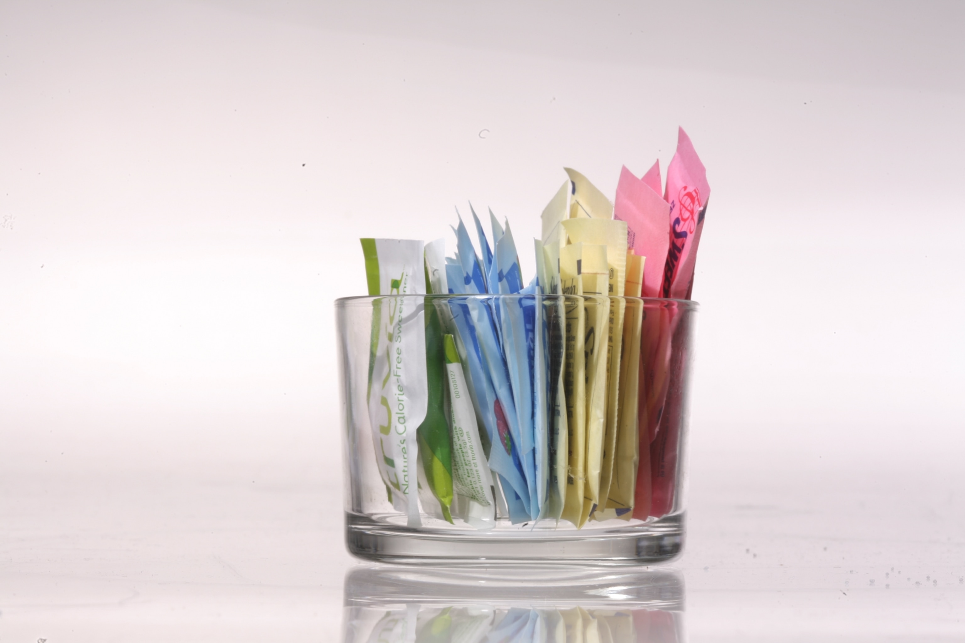A glass dish of sugar packets including sugar alternatives