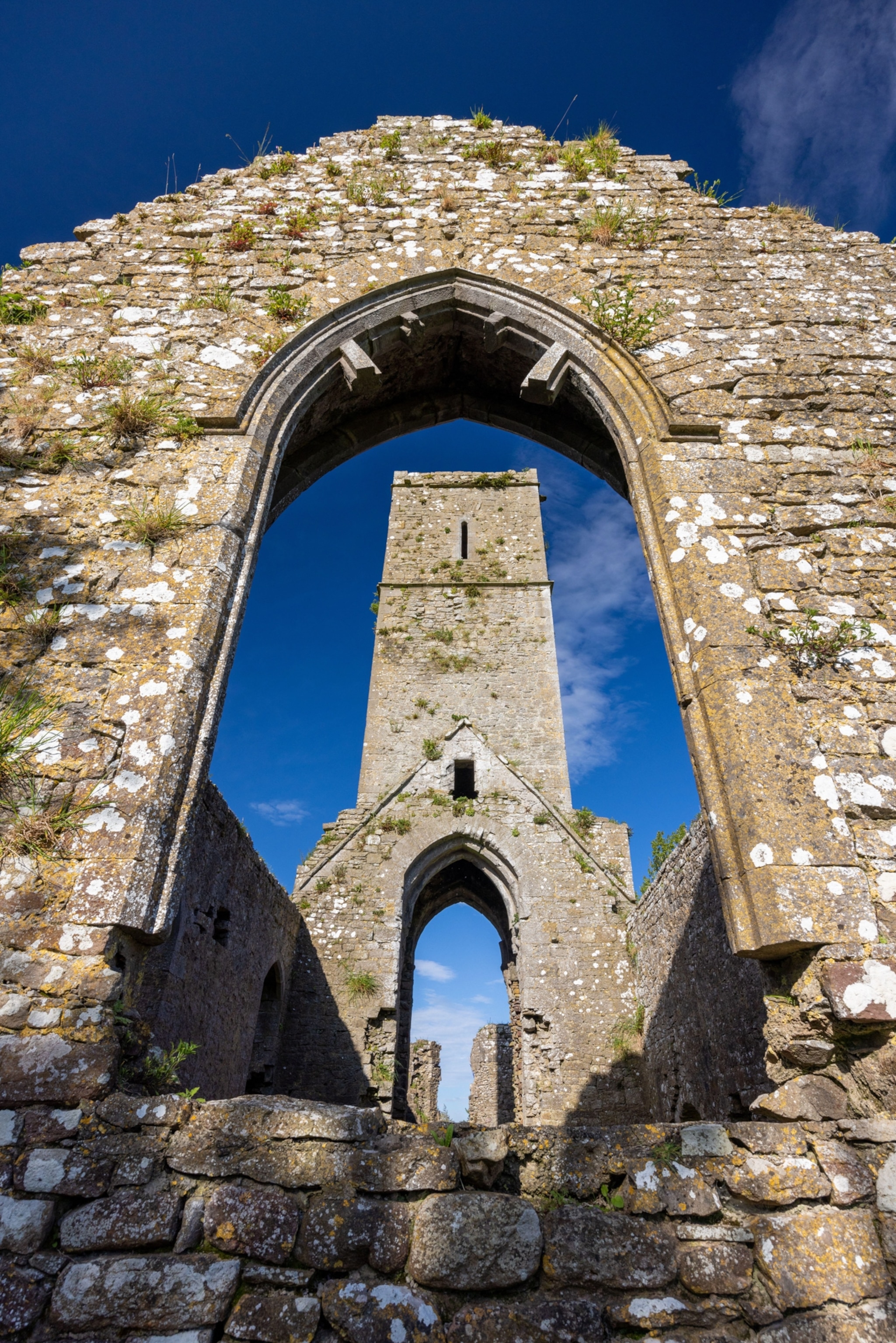 A stone archway frames a view of a stone tower, partially in ruin