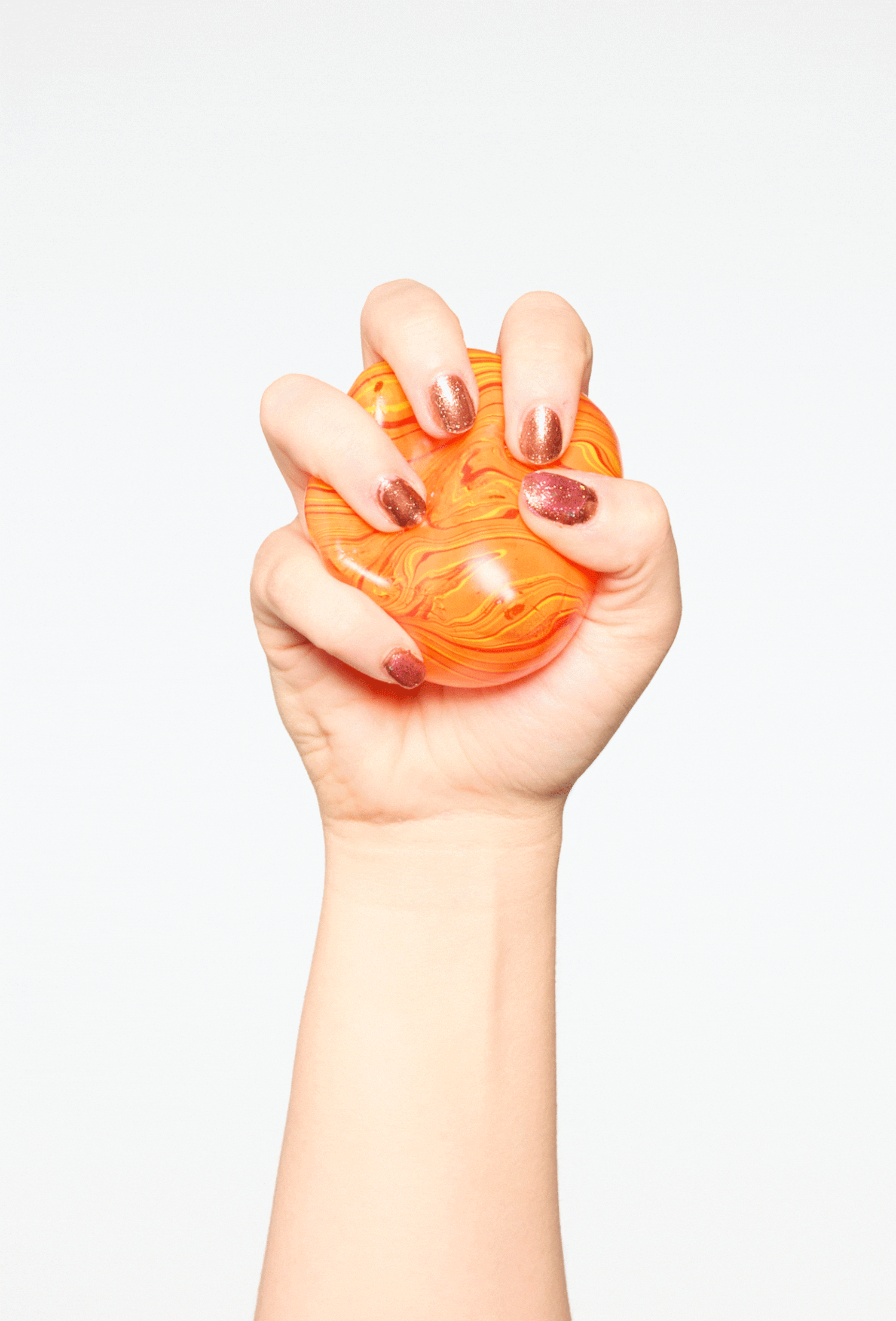 A close up of a woman's hand with painted nails squeezing an orange stress ball.