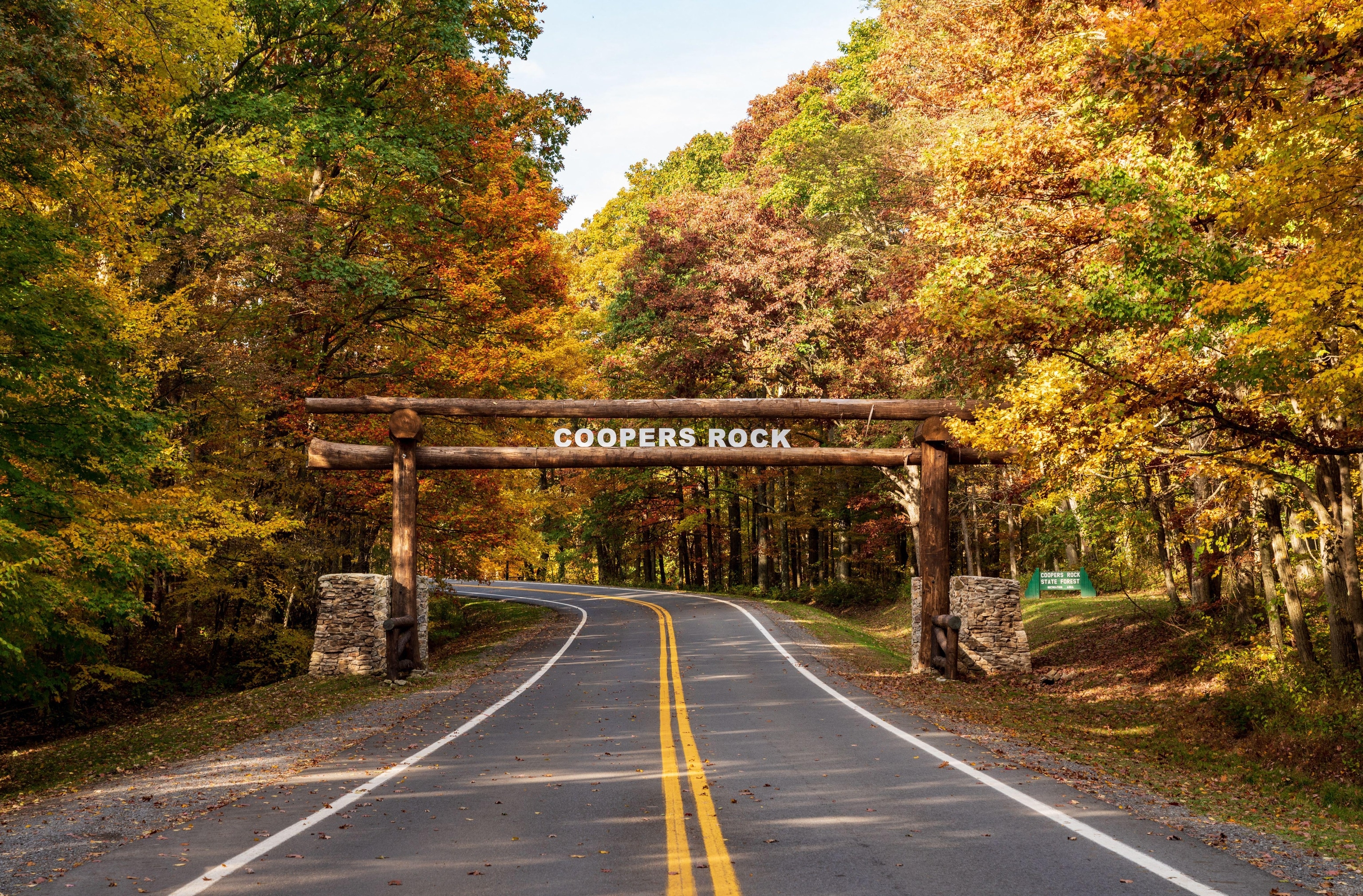 A road leading into a sign entering Coopers Rock State Forest, surrounded by trees with fall colors
