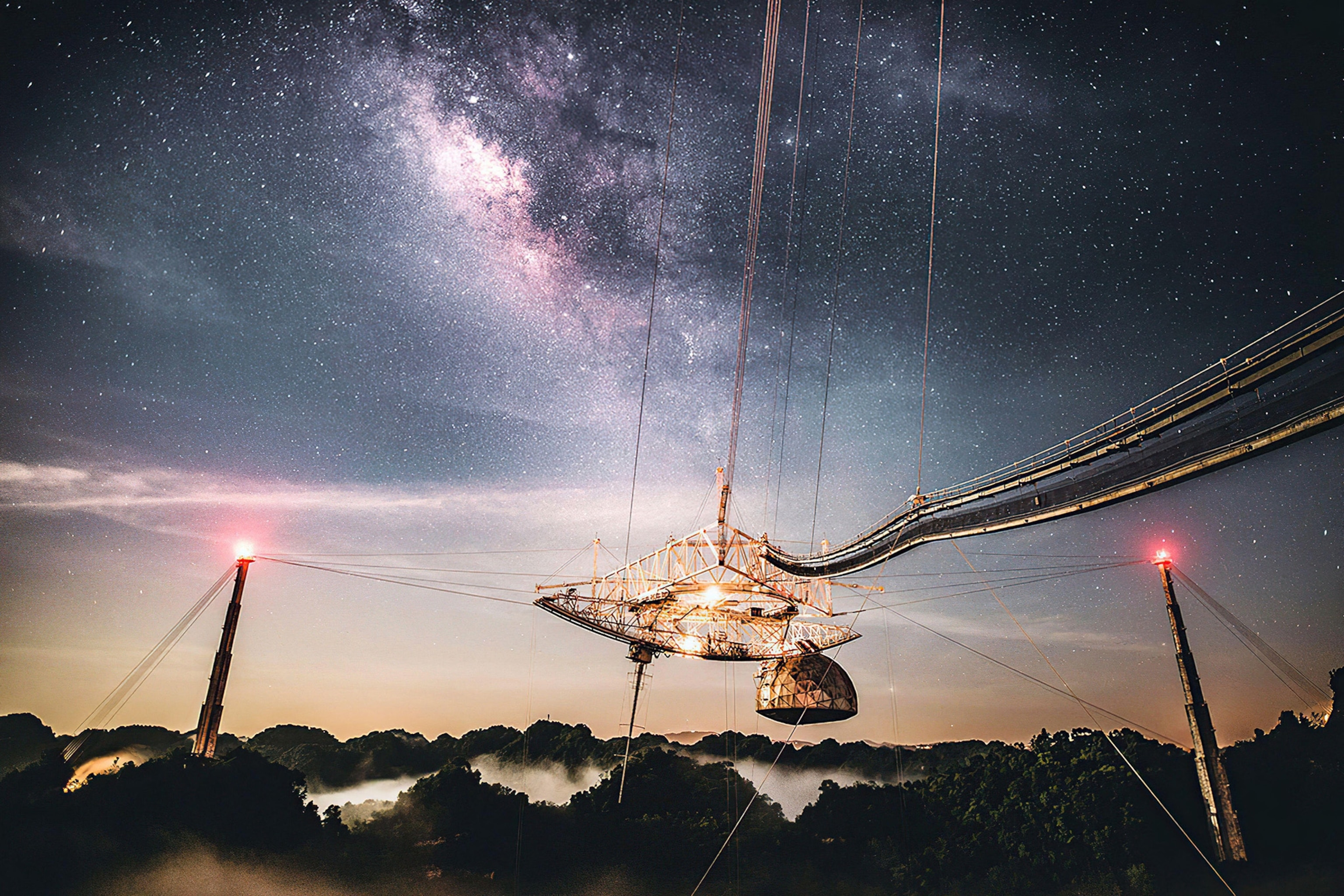 A massive telescope lit up at night in front of a view of the Milky Way.