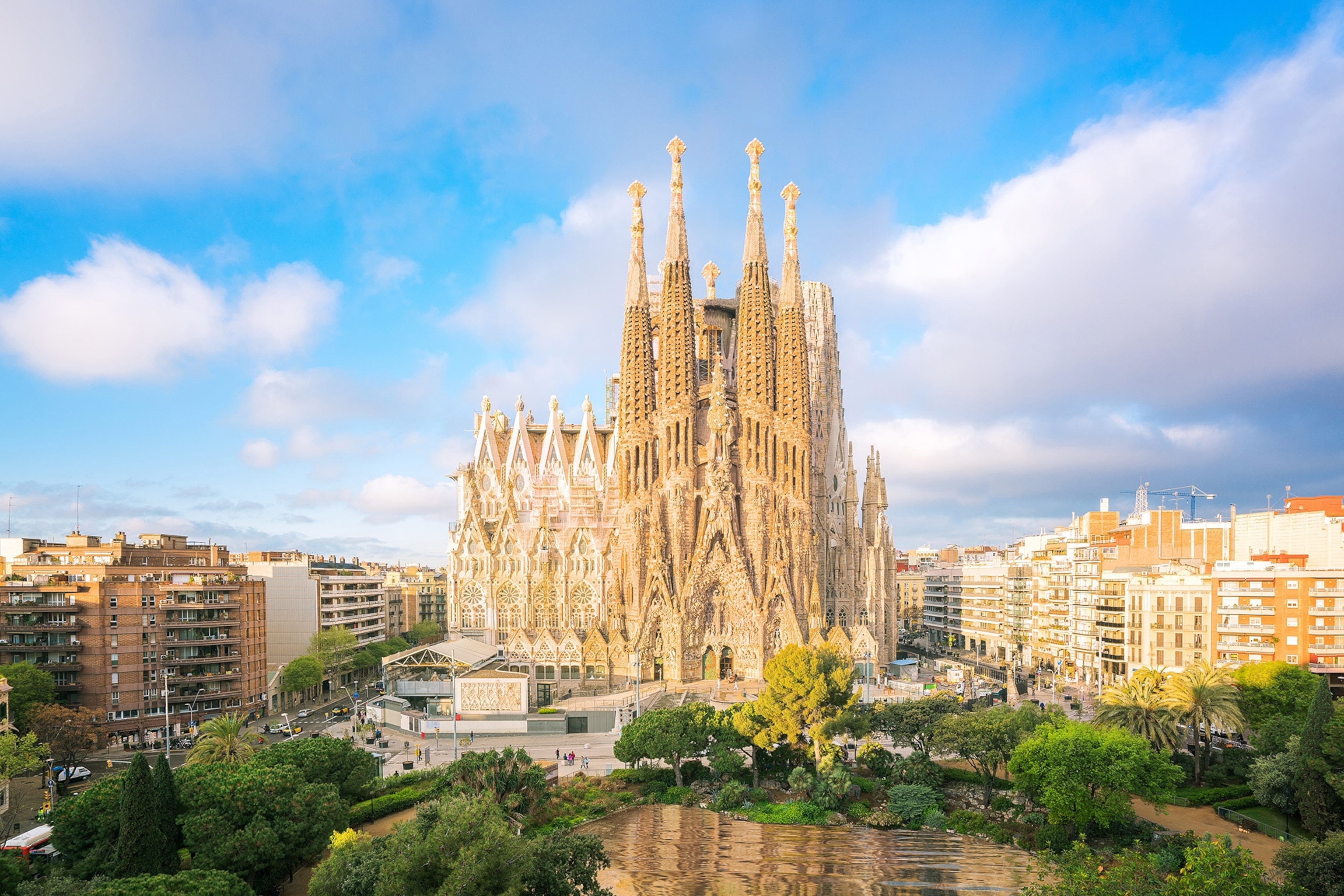 A large stone building with an intricate design against a blue, slightly cloudy sky in Barcelona.