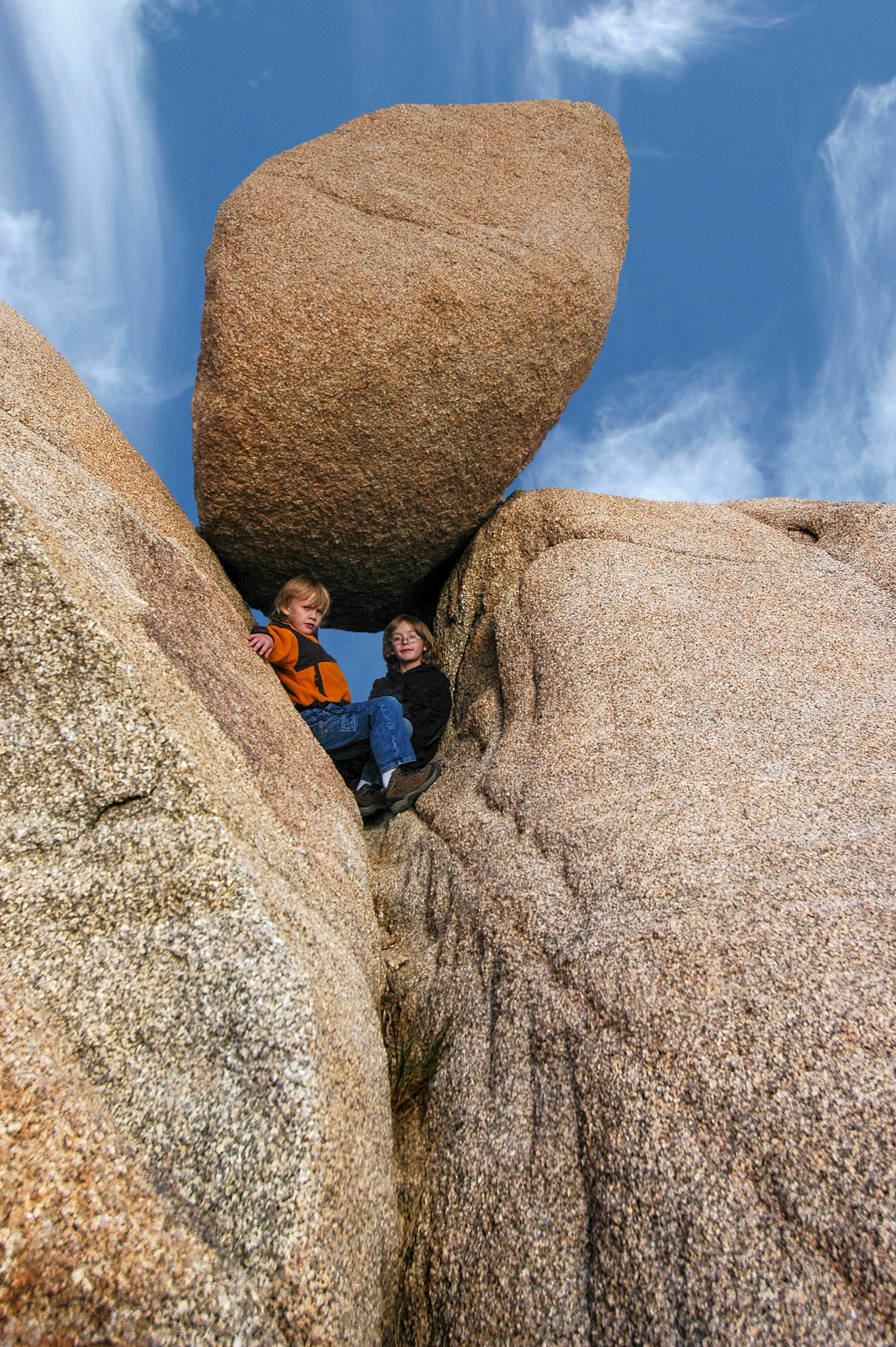 Two young boys crouch between three large boulders.