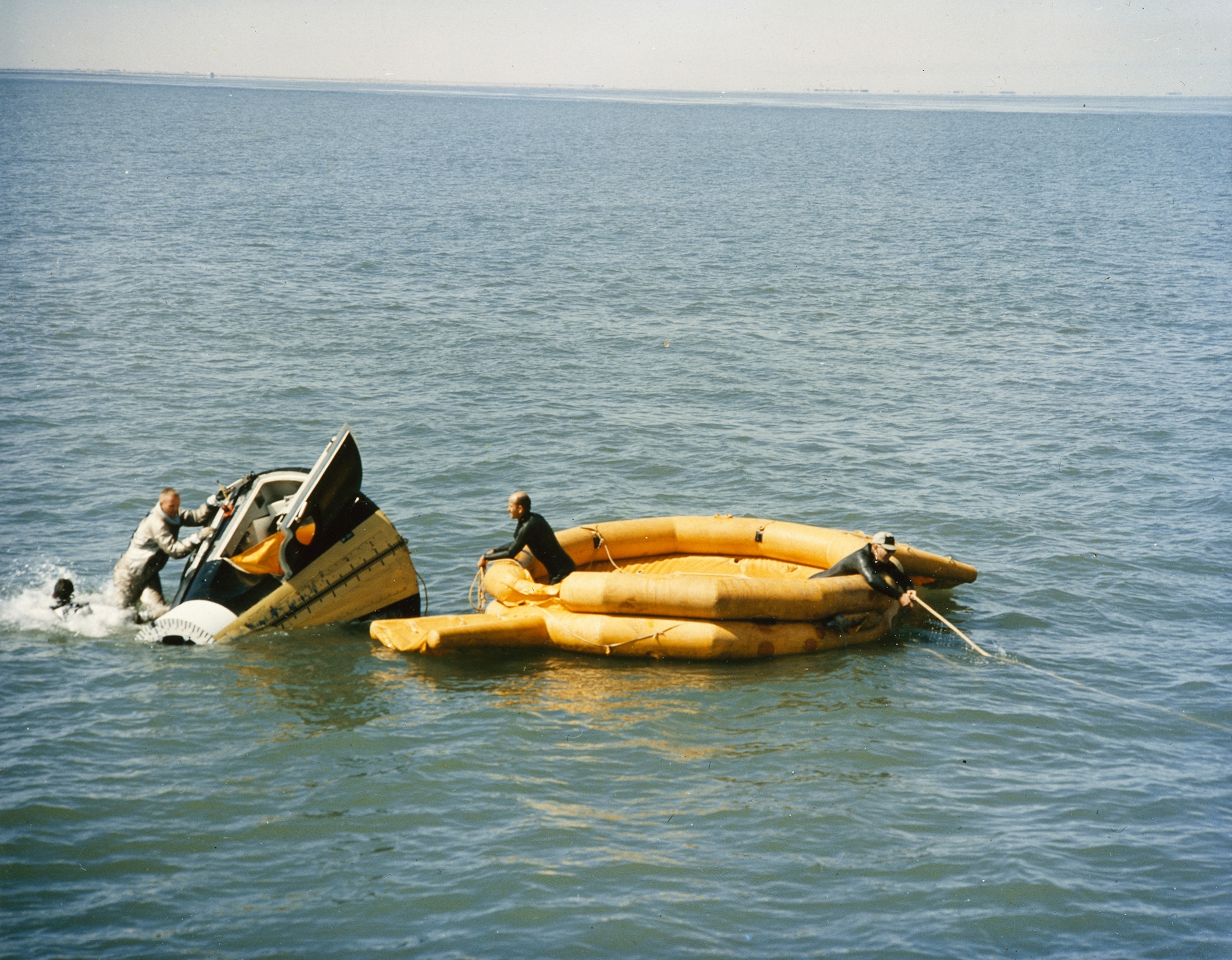 Astronauts practice exiting a spacecraft while divers stand by.
