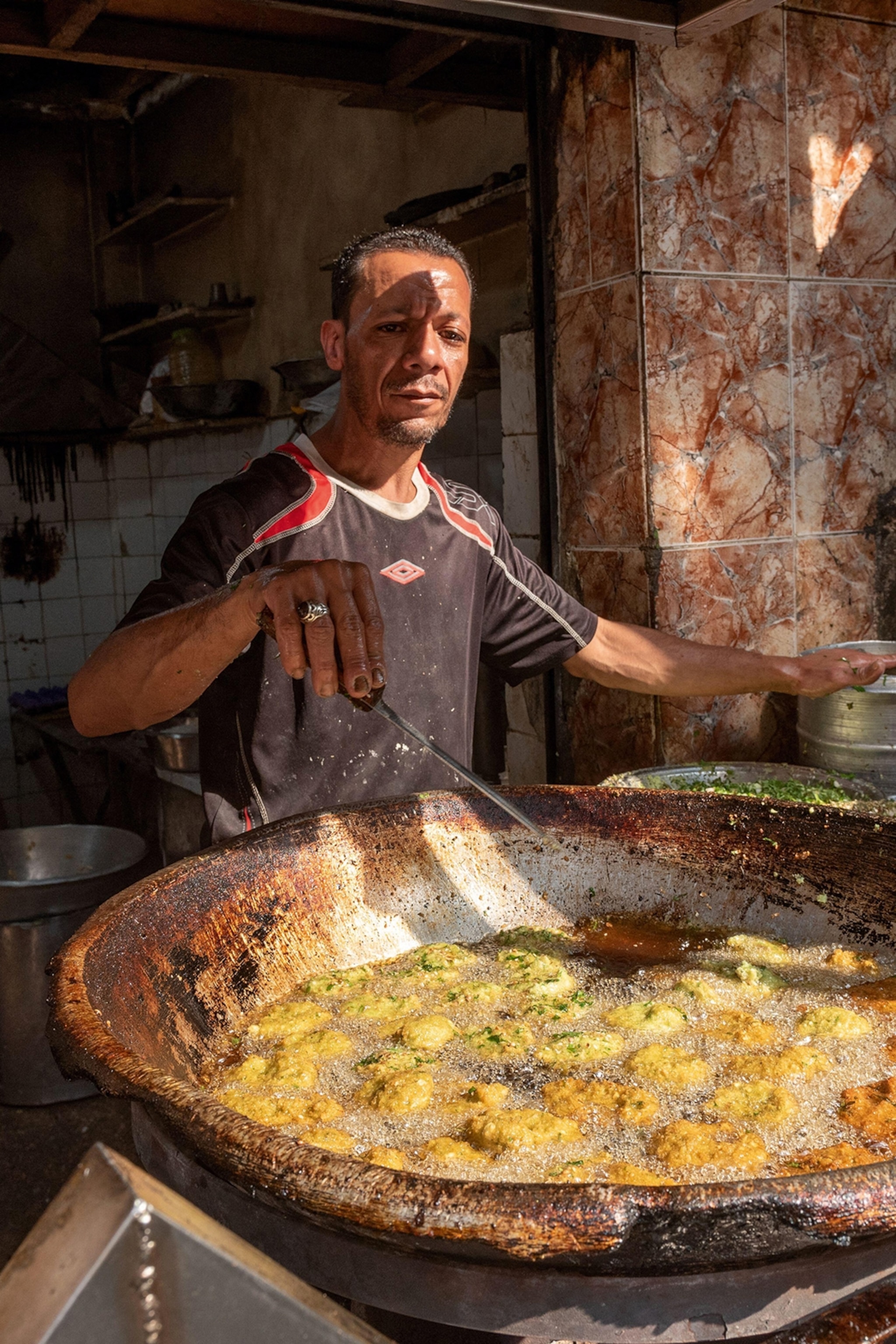 A local street food vendor dep-frying falafel in a large stone wok.