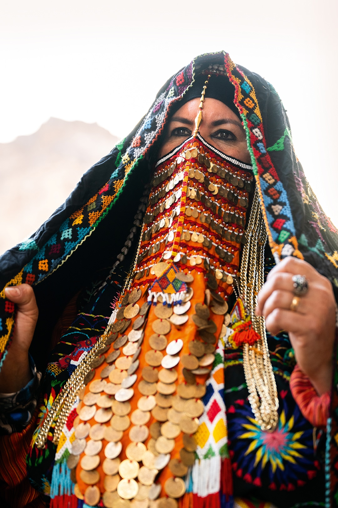 A portrait of a woman wearing colourful head and face garments.
