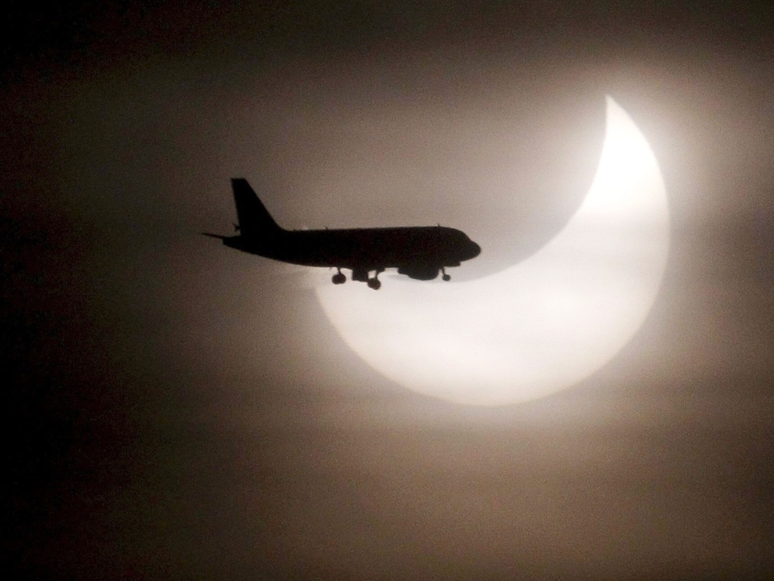 An airplane silhouetted against an eclipsed sun (picture).