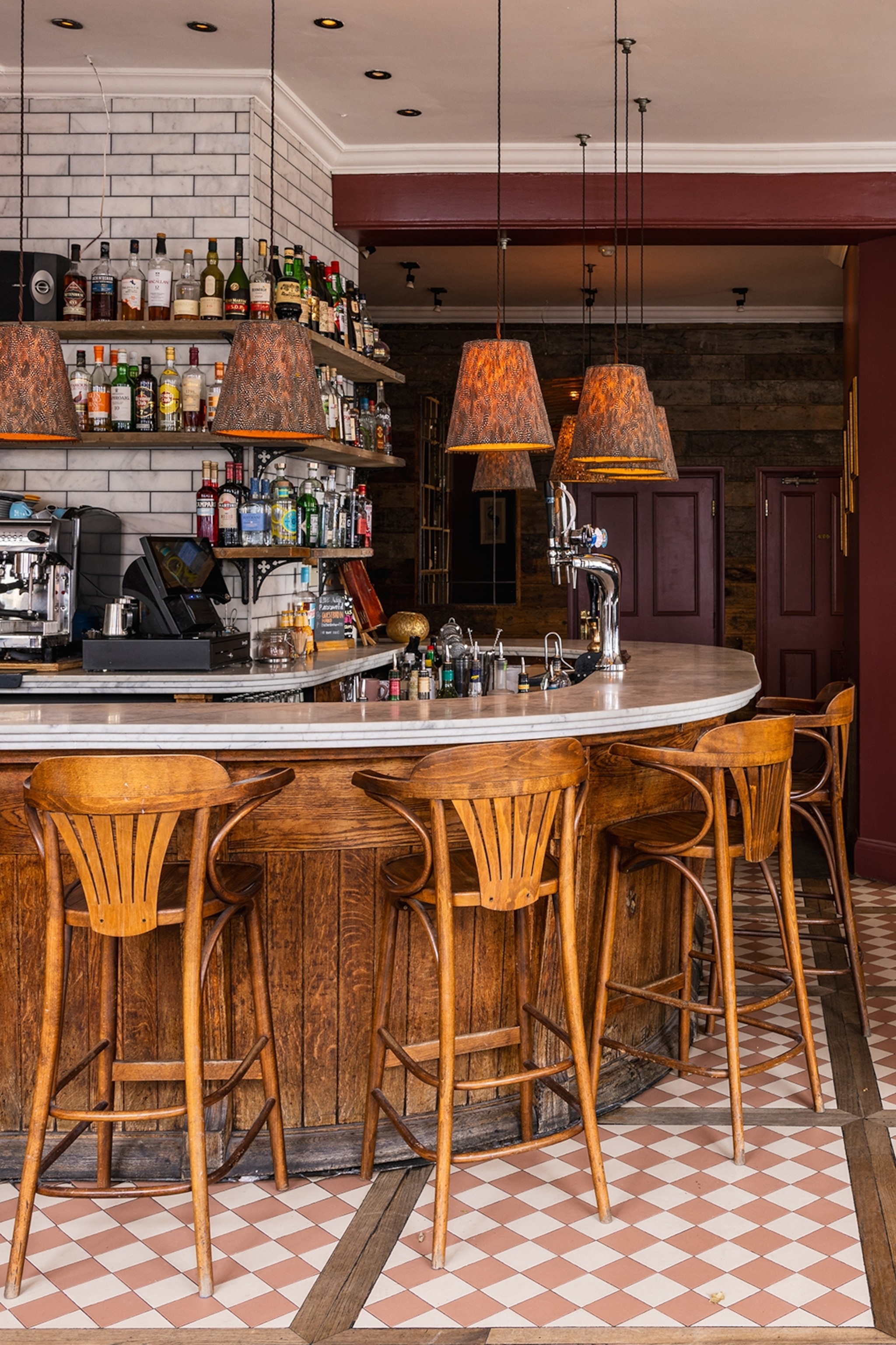 The horseshoe bar of a pub with tiled floor and high chairs.