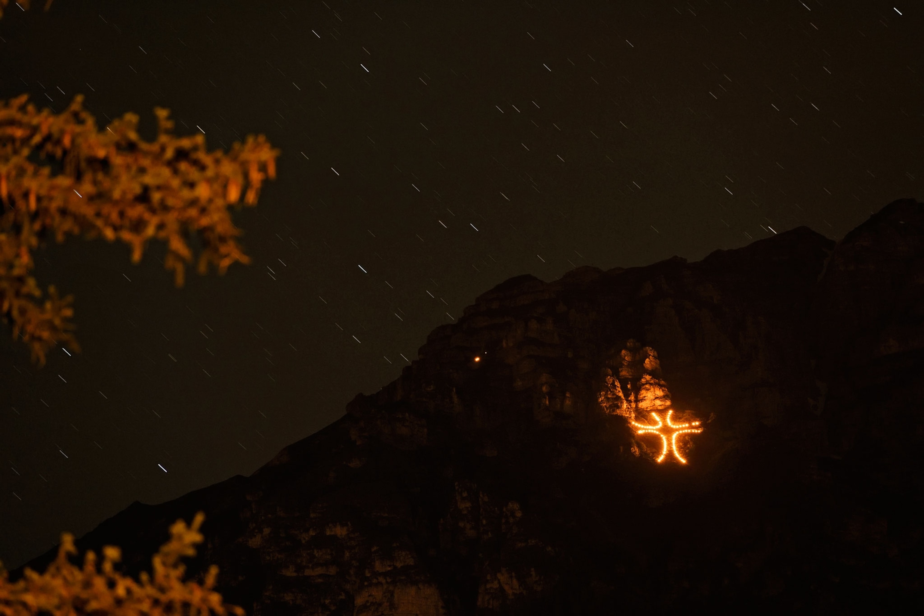 a cross lit up by fire on a mountainside