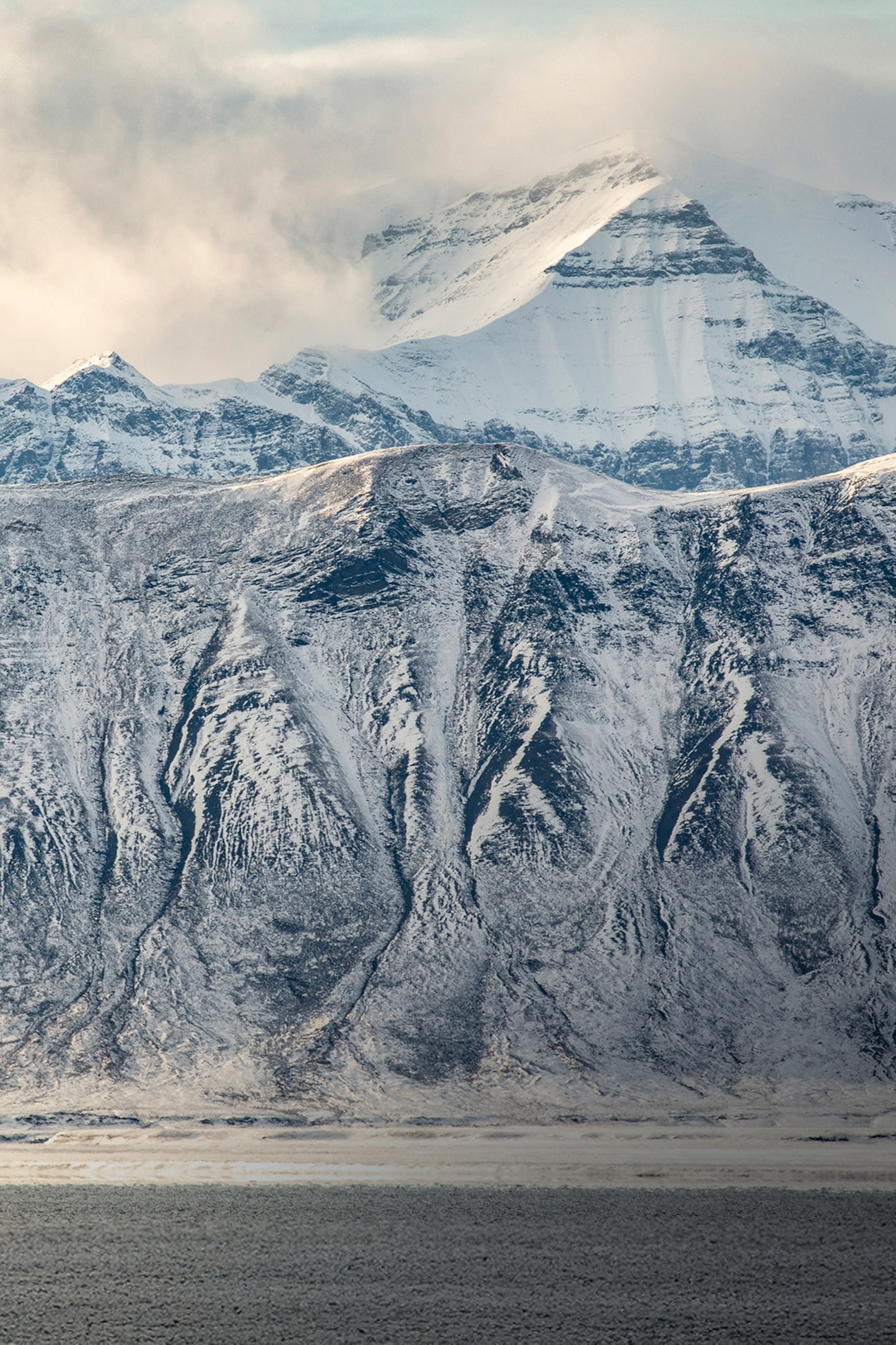 A snow-covered and impressive mountain range rising from the shore of an artic sea.