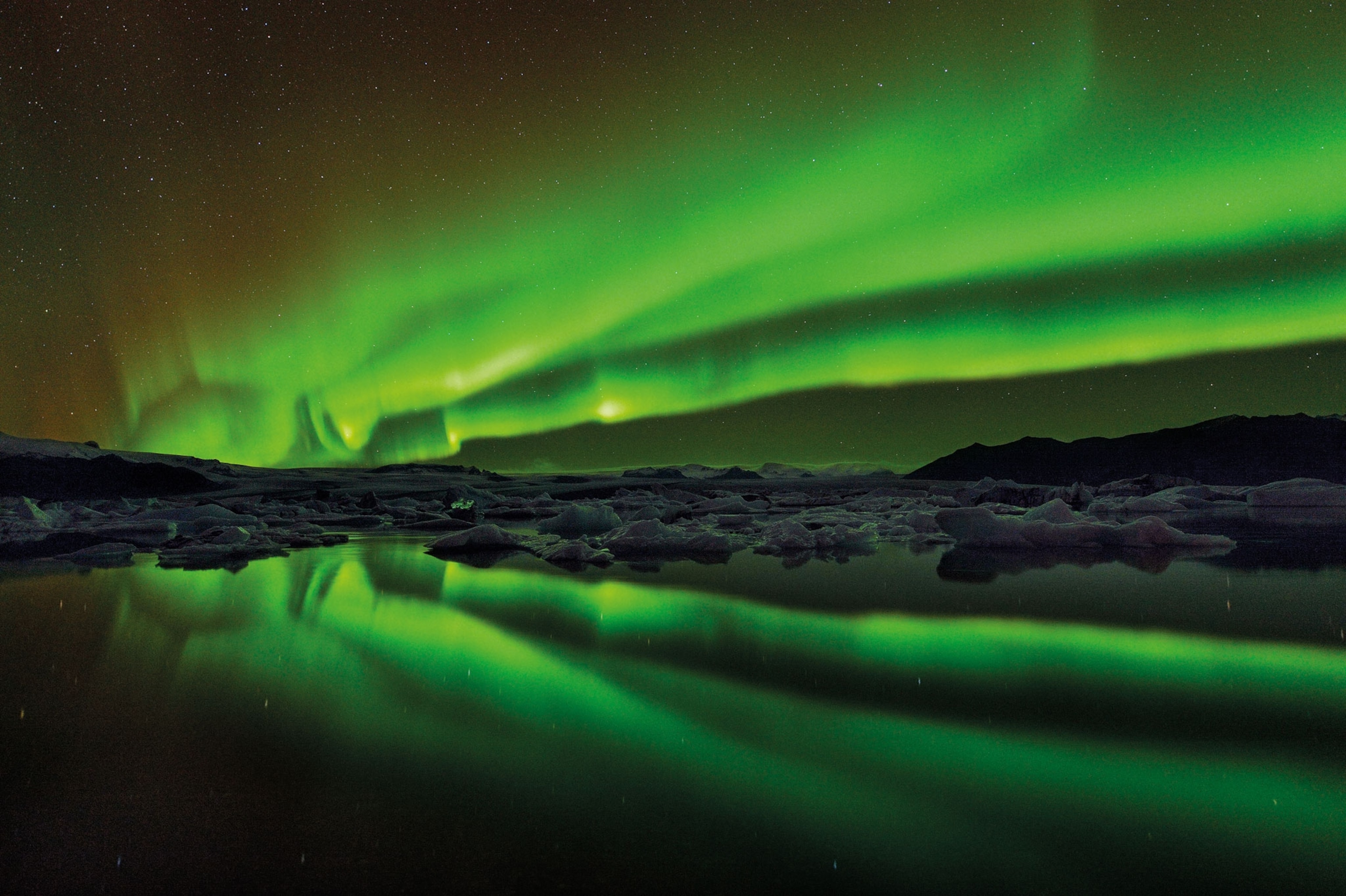 Ice on a lake under the glow of a green aurora borealis.