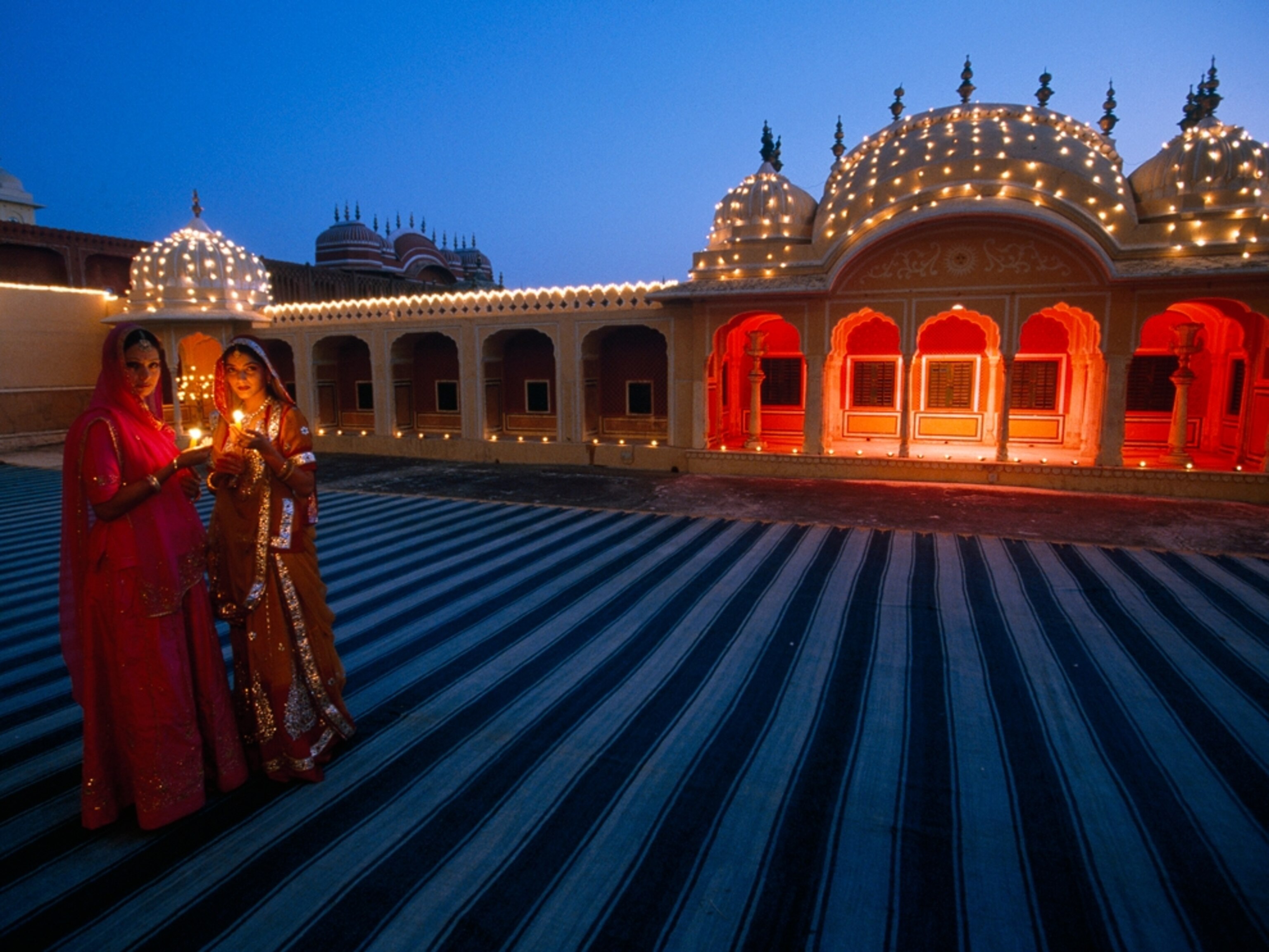 Women holding candles in front of a lit palace