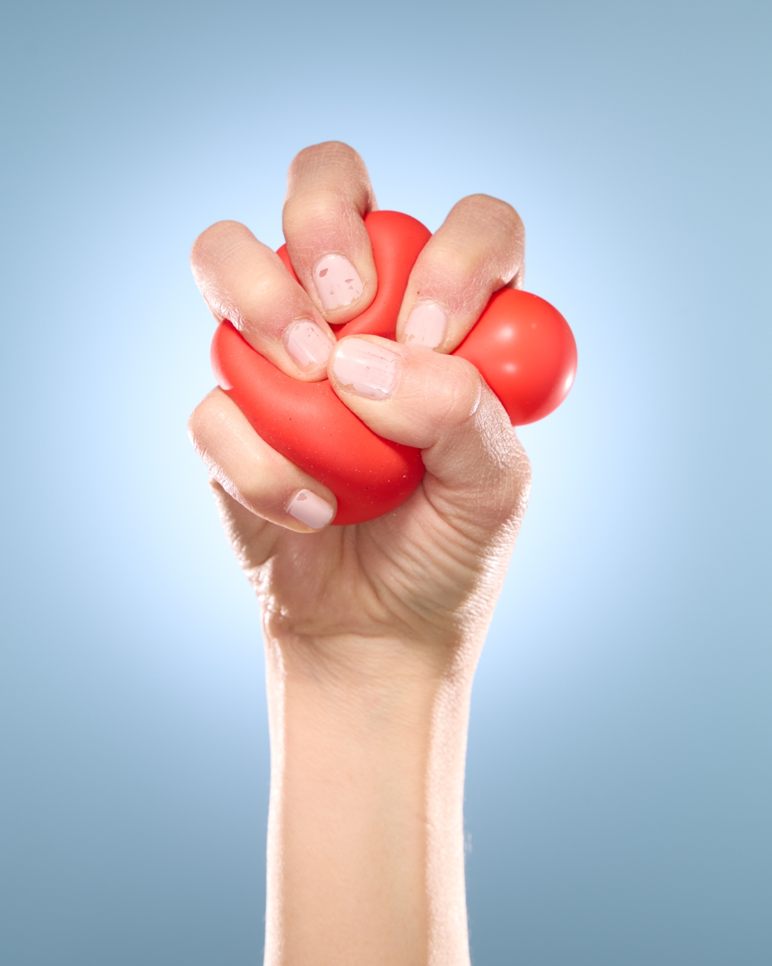 A hand tightly gripping a stress ball, which is bulging from the pressure