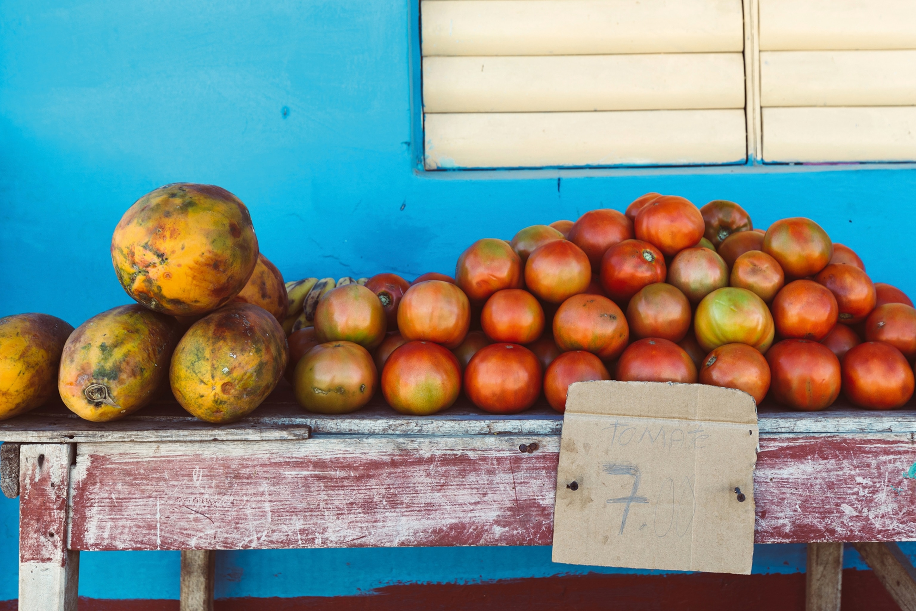 A simple wooden bench with stacked tomatoes perched up against a house wall.